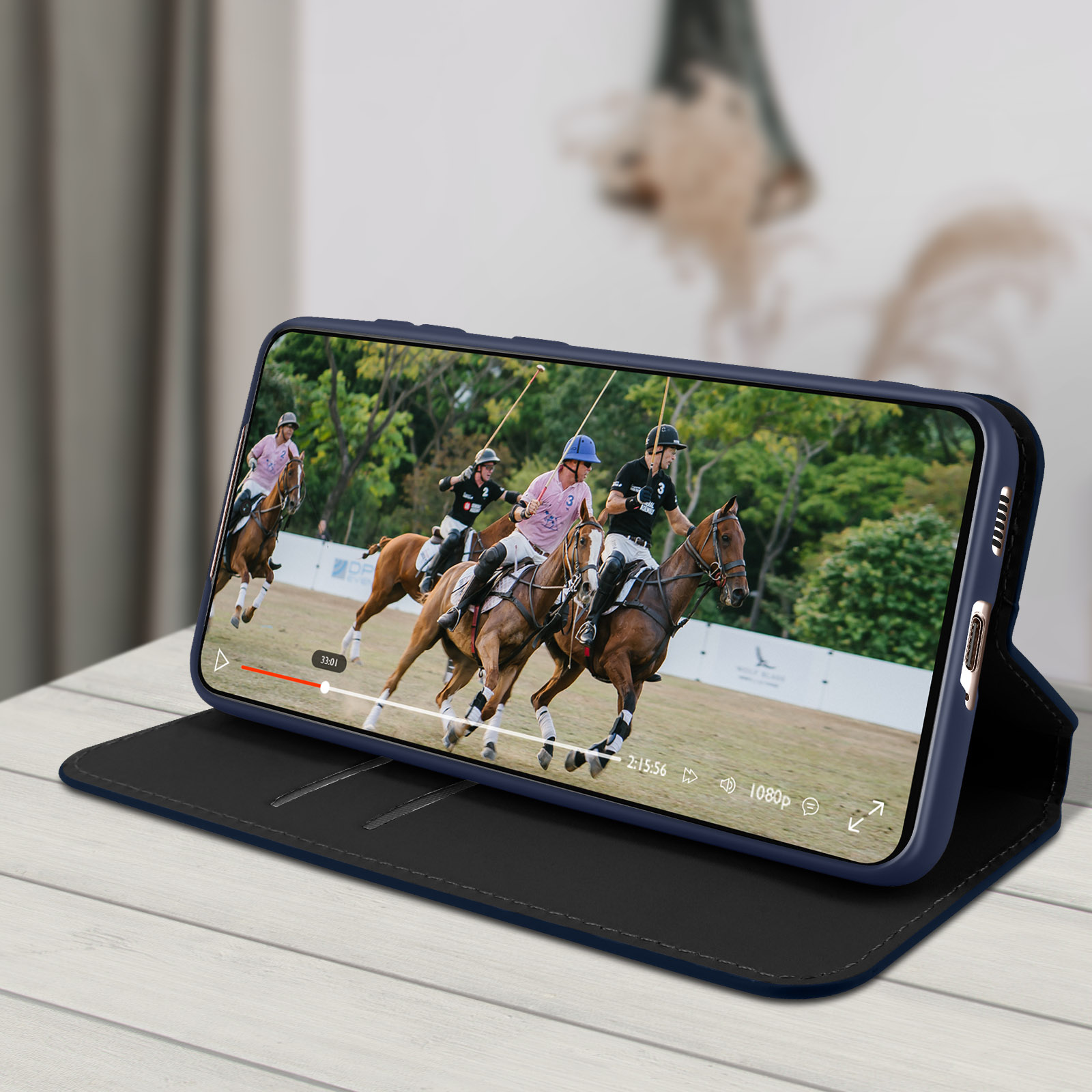 Un telefono mostra una partita di polo. Il telefono è in una custodia blu, su un tavolo di legno bianco.