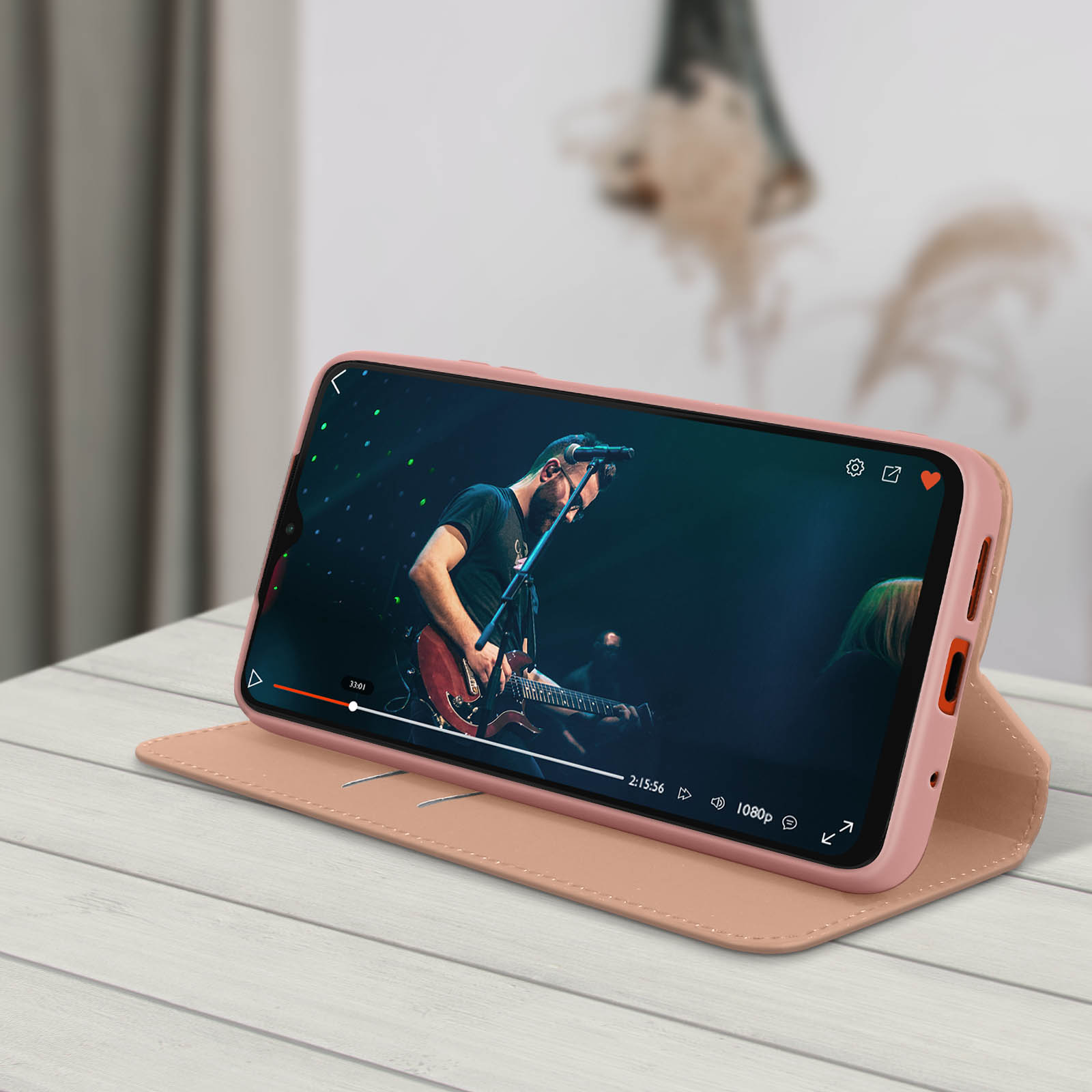 Custodia per telefono rosa con un telefono che mostra un video di un concerto. La custodia è aperta su un tavolo di legno.