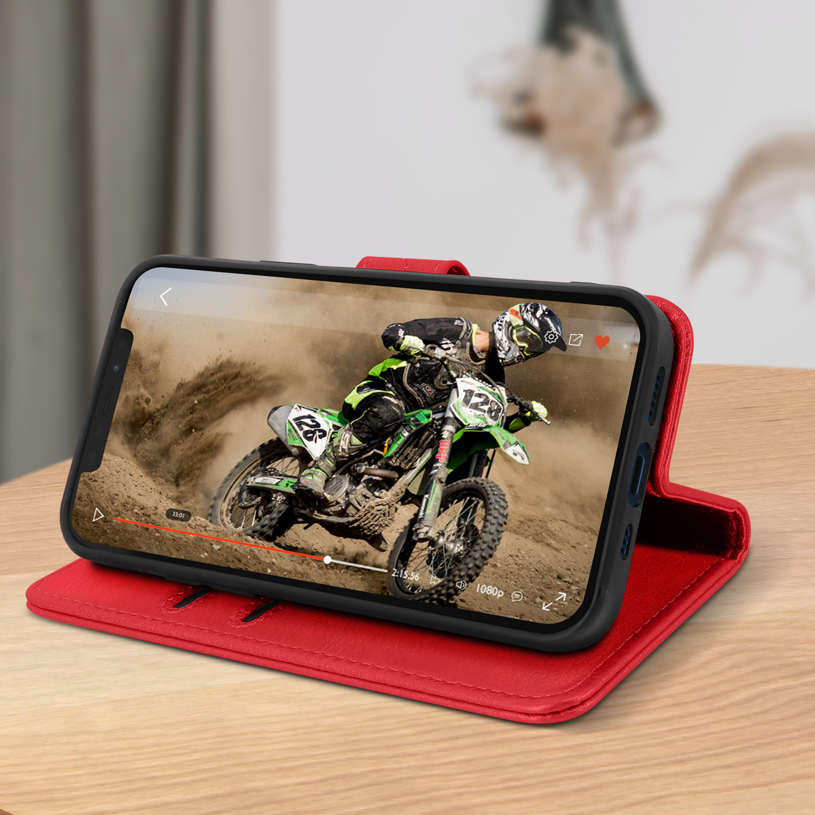 Étui de téléphone rouge avec téléphone ouvert, montrant une vidéo d'un pilote de motocross. Table en bois, flou.