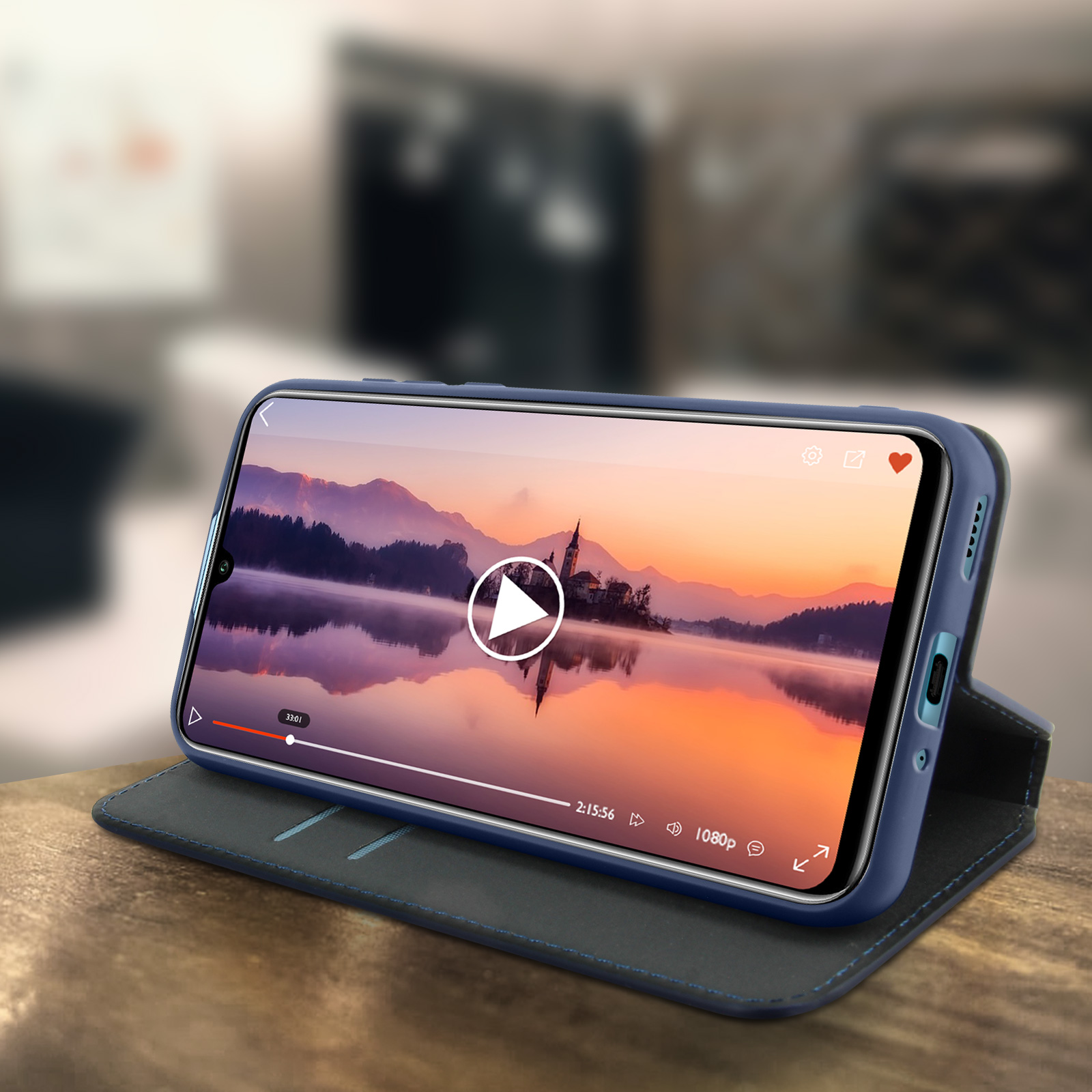Telefono in custodia blu, mostra video, su un tavolo di legno. Sfondo sfocato.