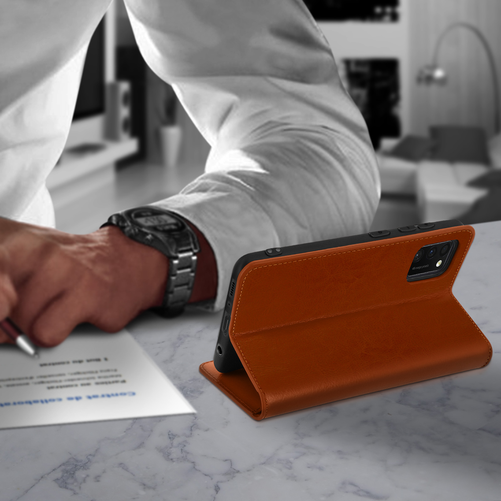 Un étui de téléphone sur une table. Une personne écrit en arrière-plan. L'étui est marron.