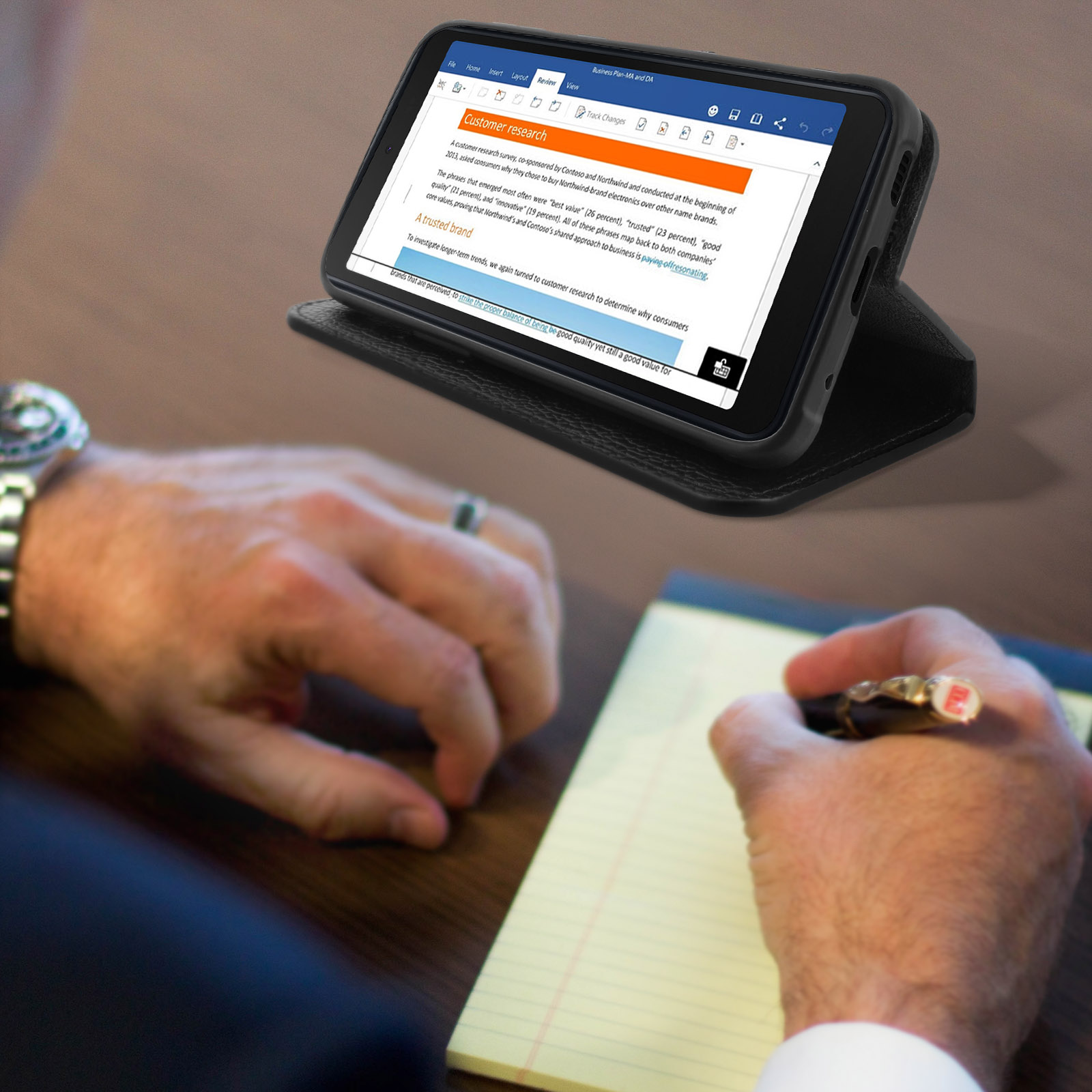 Un téléphone affichant un document sur un bureau, une personne écrit avec un stylo.