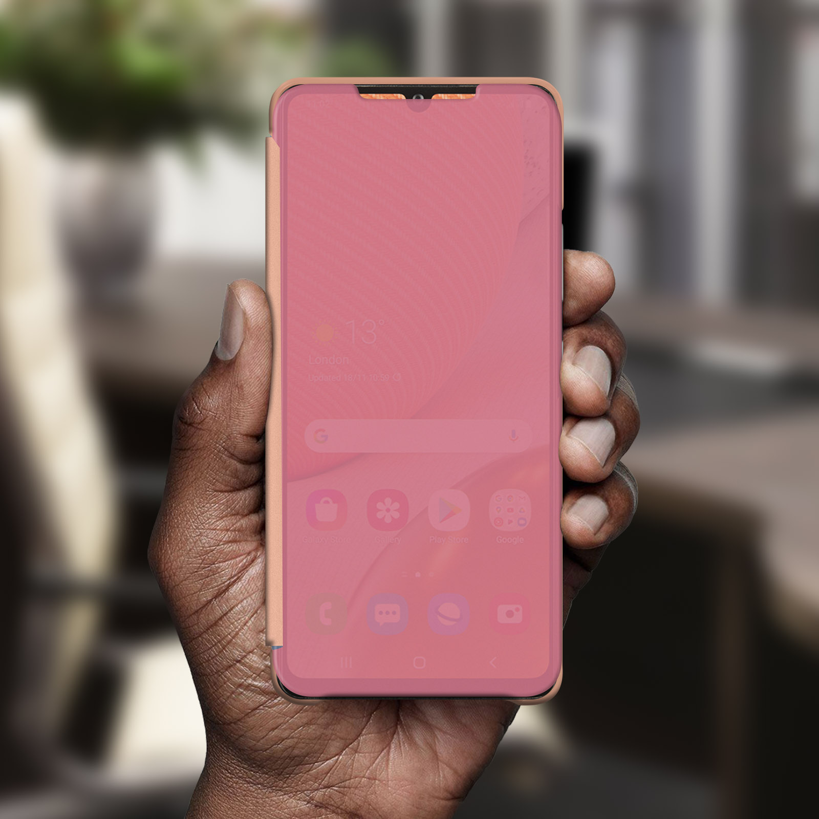 Mano sosteniendo teléfono en funda rosa. Pantalla muestra pantalla rosa con iconos de aplicaciones.