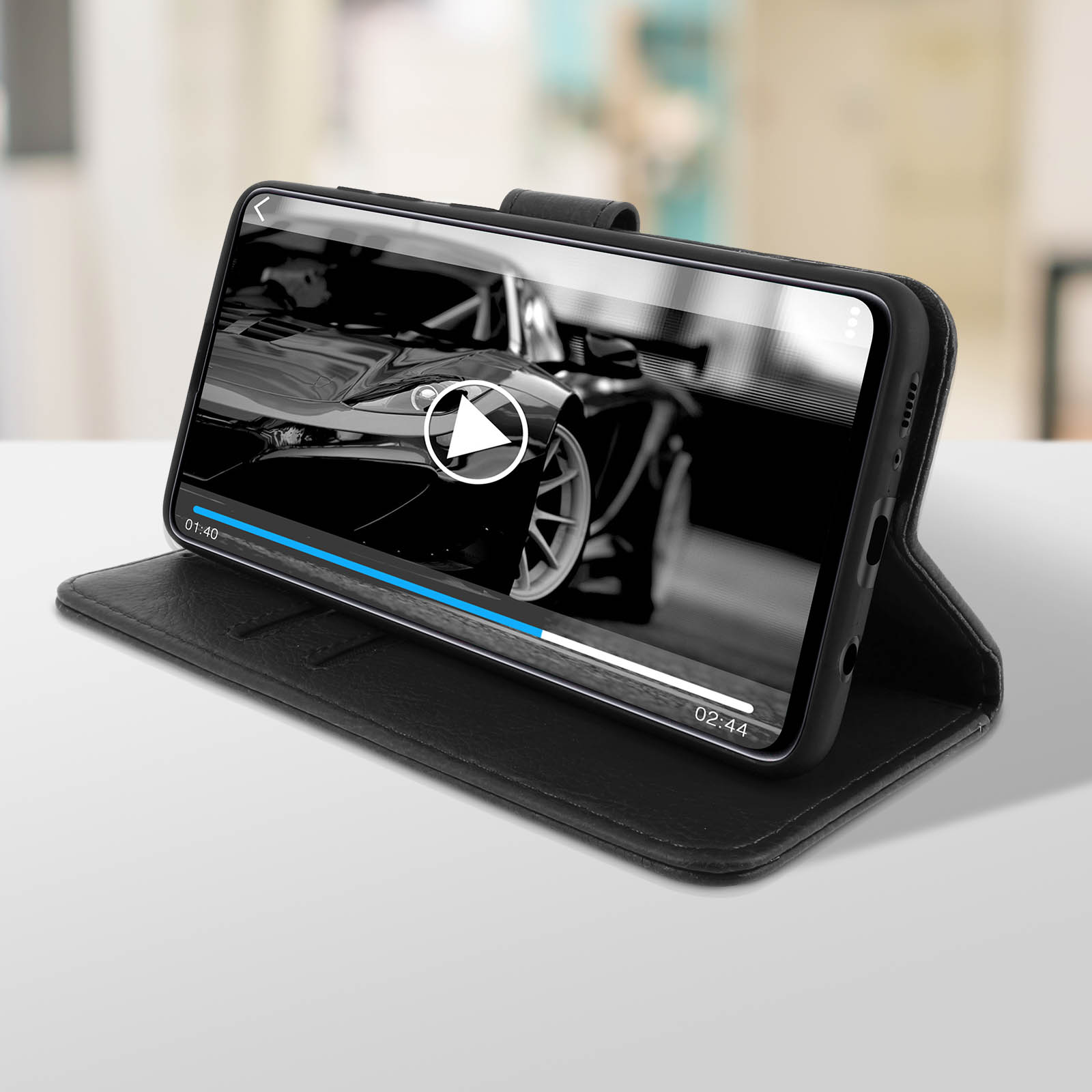Étui de téléphone noir avec un téléphone affichant une vidéo. Le téléphone est posé sur une table blanche.