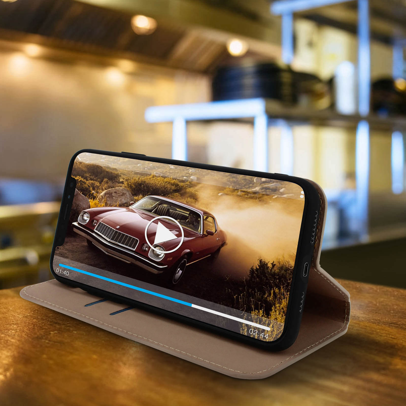 Telefoon op houten tafel toont video van rode klassieke auto met afspeelknop.
