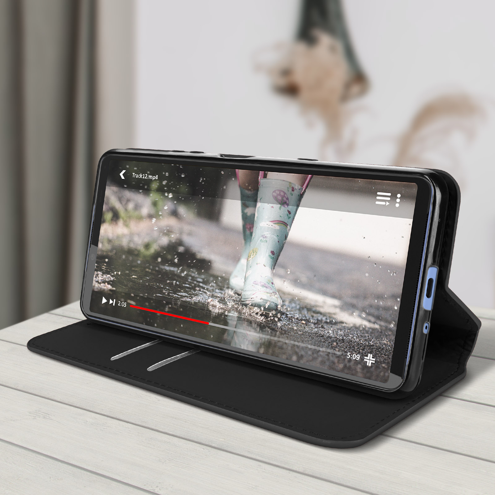 Custodia per telefono nera aperta, che mostra un telefono che riproduce un video. La custodia è appoggiata su legno.