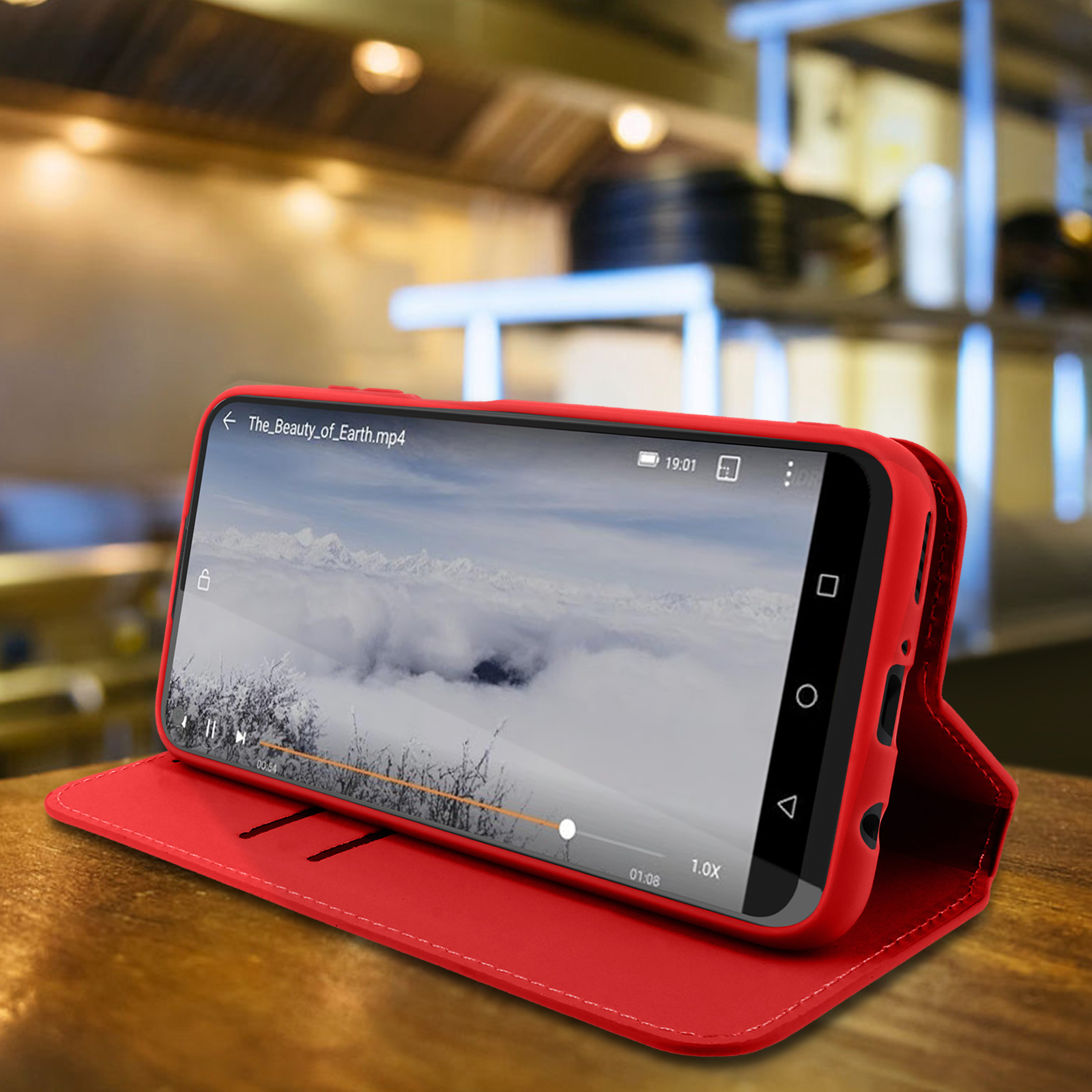 Custodia rossa per telefono aperta su superficie in legno, riproduce un video. Sfondo: cucina.