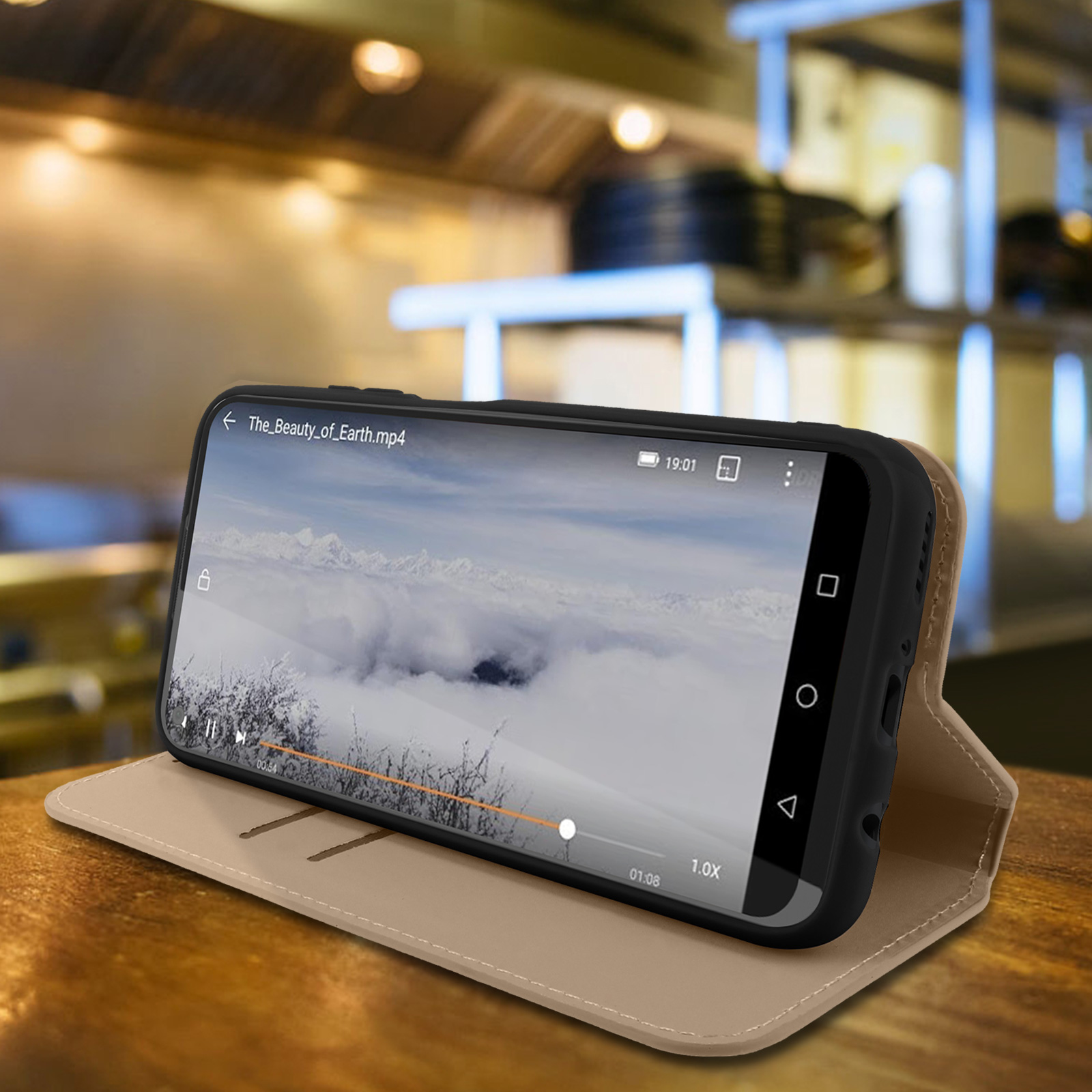 Een telefoon in een beige hoes staat op een oppervlak en toont een video van wolken. De hoes is open.