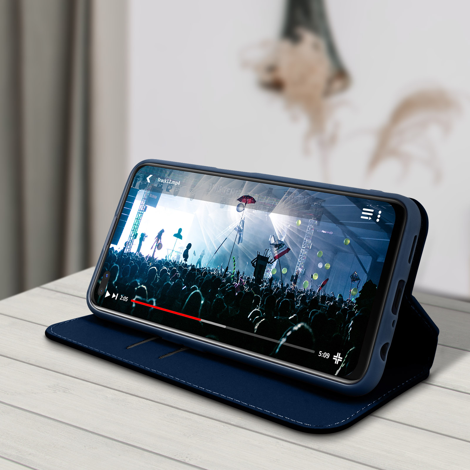 Un telefono in una custodia blu che riproduce un video di un concerto. La custodia è aperta e su una superficie.