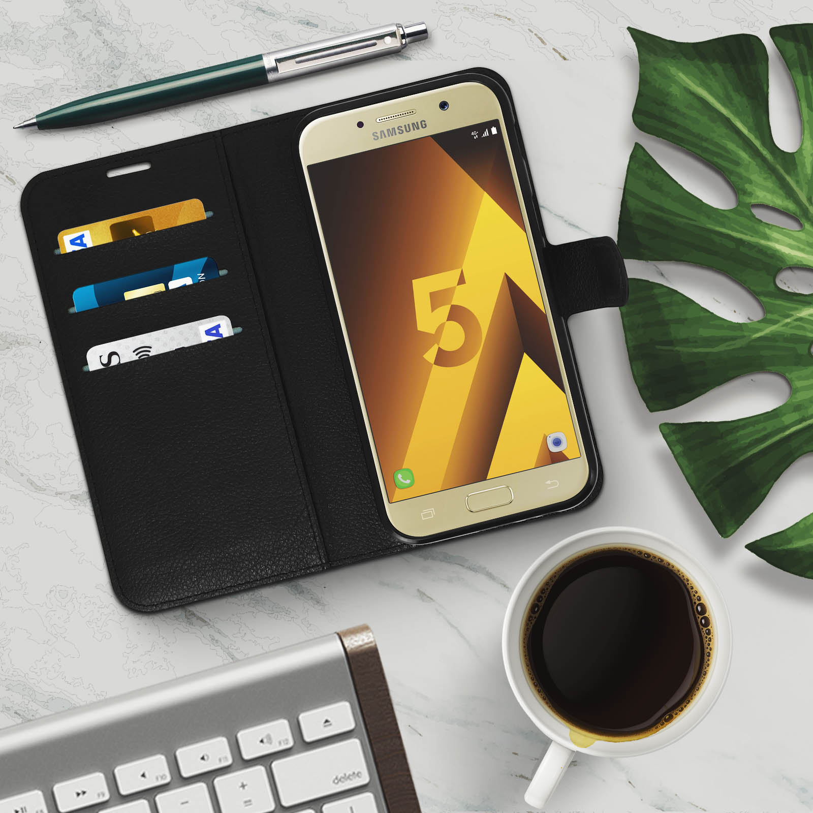 Telefono in una custodia nera con carte e penna. Caffè e tastiera su una superficie di marmo.