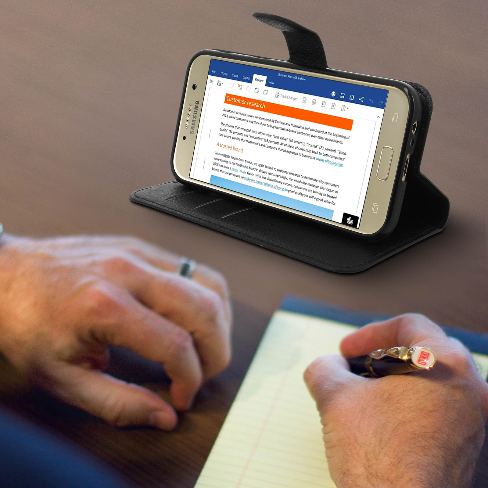 Un telefono mostra un documento. Una persona scrive su un blocco note con una penna.