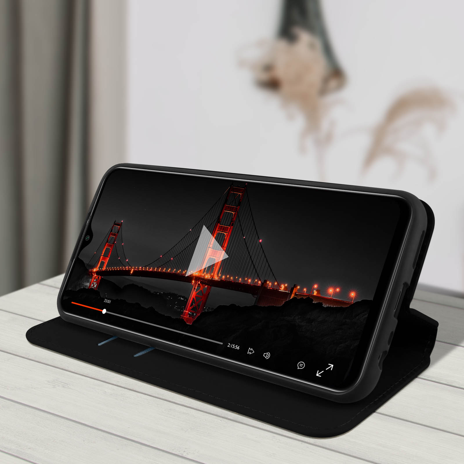 Téléphone montrant une vidéo du Golden Gate la nuit. Étui de téléphone noir sur un bureau.
