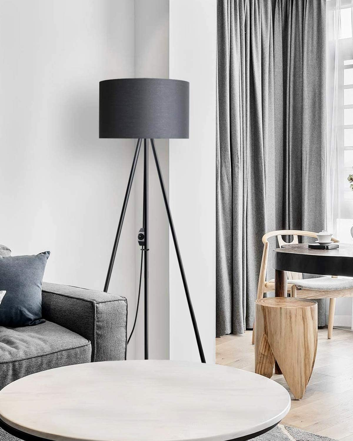 Ein Wohnzimmer mit Stehlampe, Sofa, rundem Tisch und Vorhängen. Die Lampe hat ein schwarzes Gestell.