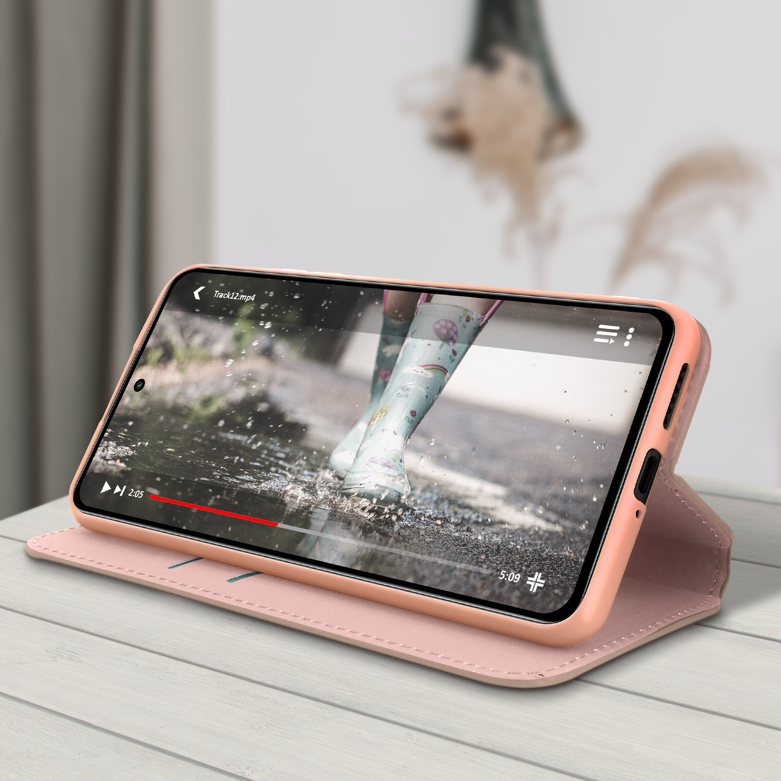 Un telefono in una custodia rosa mostra un video. Il video mostra piedi con stivali che camminano in una pozzanghera. La custodia è aperta.