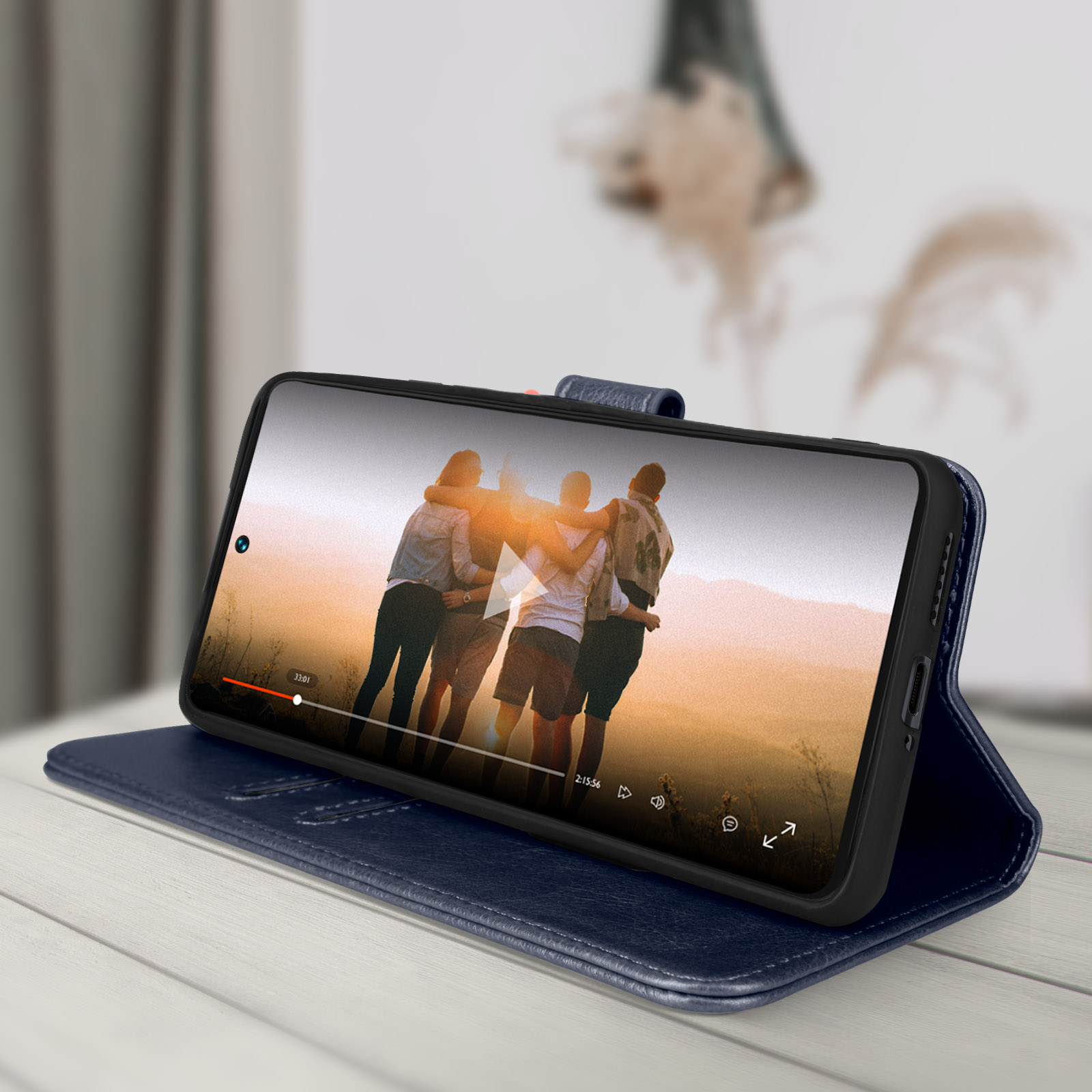 Een telefoon in een blauwe hoes toont een video van mensen. De telefoon staat op een blauwe boekachtige standaard.