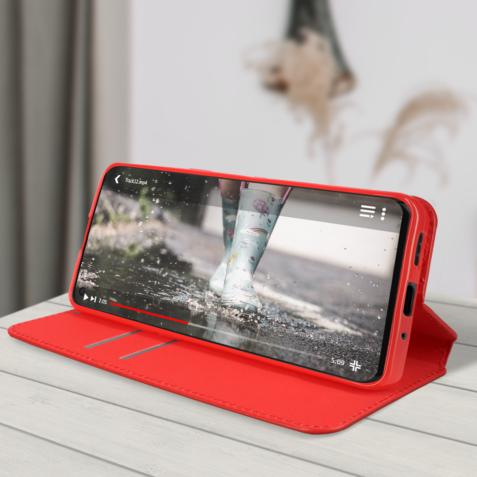 Custodia rossa aperta, con un telefono che mostra un video. Tavolo di legno, sfondo sfocato.