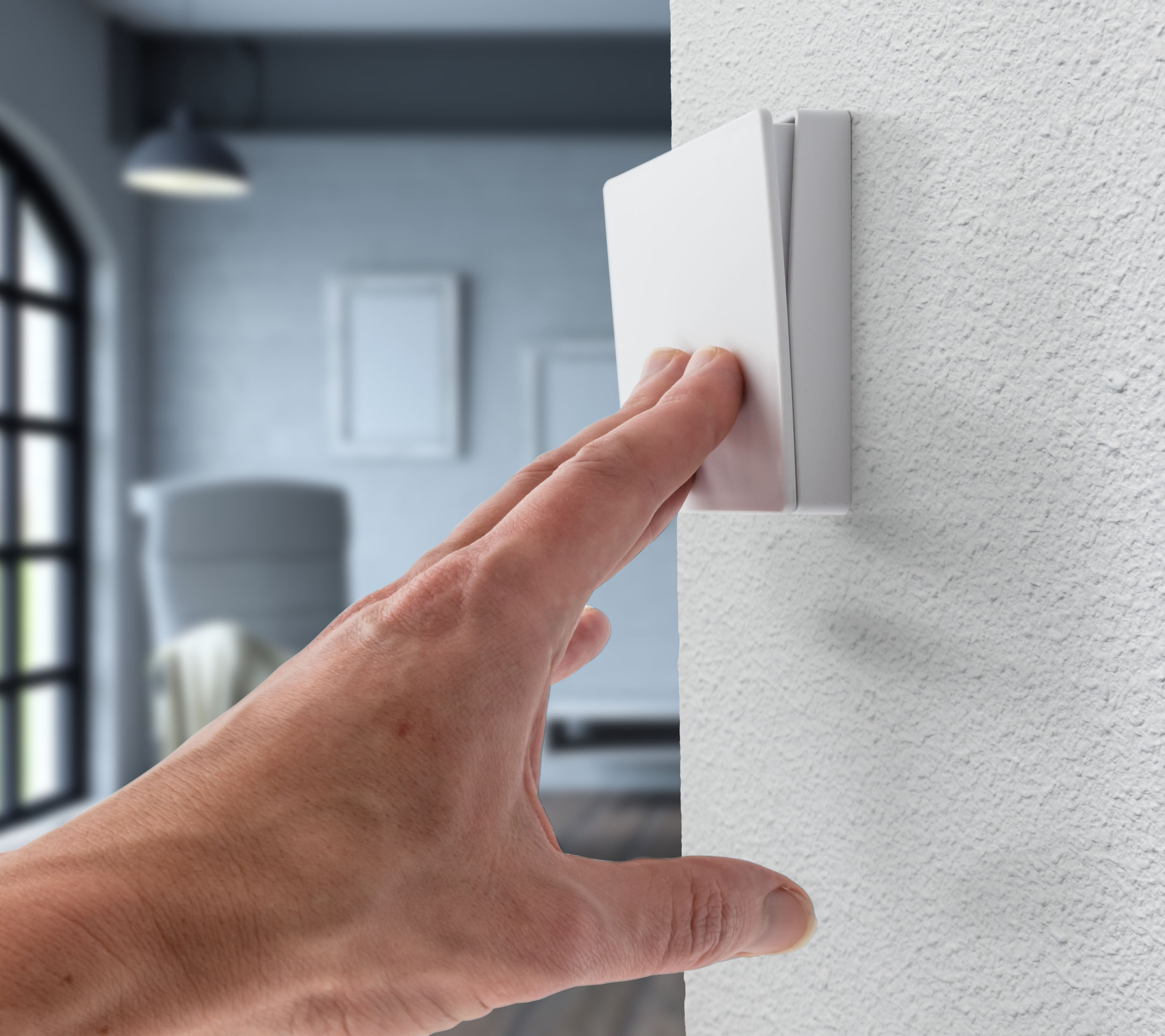 Eine Hand, die sich danach ausstreckt, einen weißen Lichtschalter an einer Wand zu betätigen.