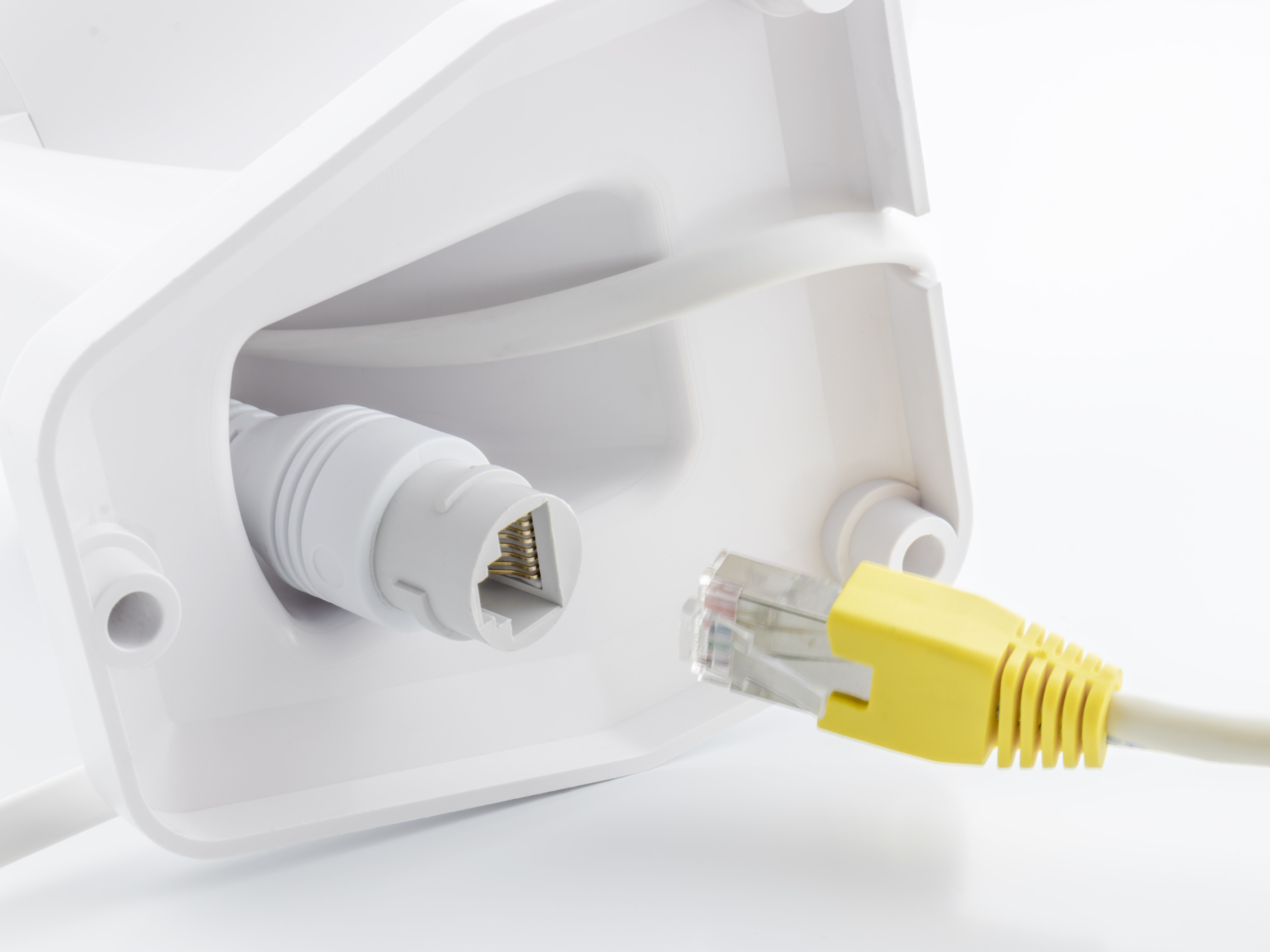 Nahaufnahme einer weißen Wand mit angeschlossenem Netzwerkkabel. Das Kabel ist gelb. Der Stecker ist grau.