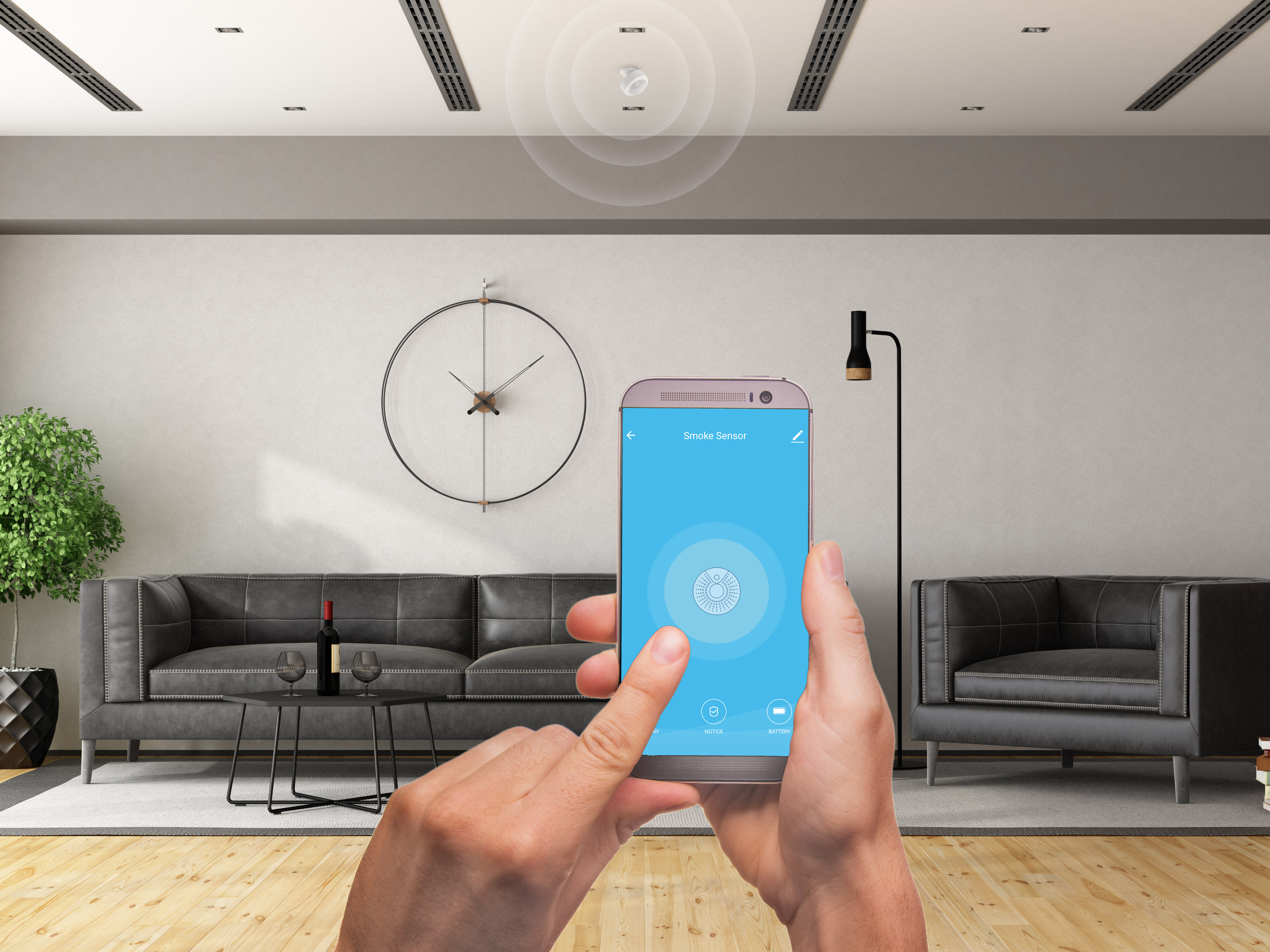 Person hält Telefon, zeigt eine App an. Rauchmelder an der Decke. Modernes Wohnzimmer.