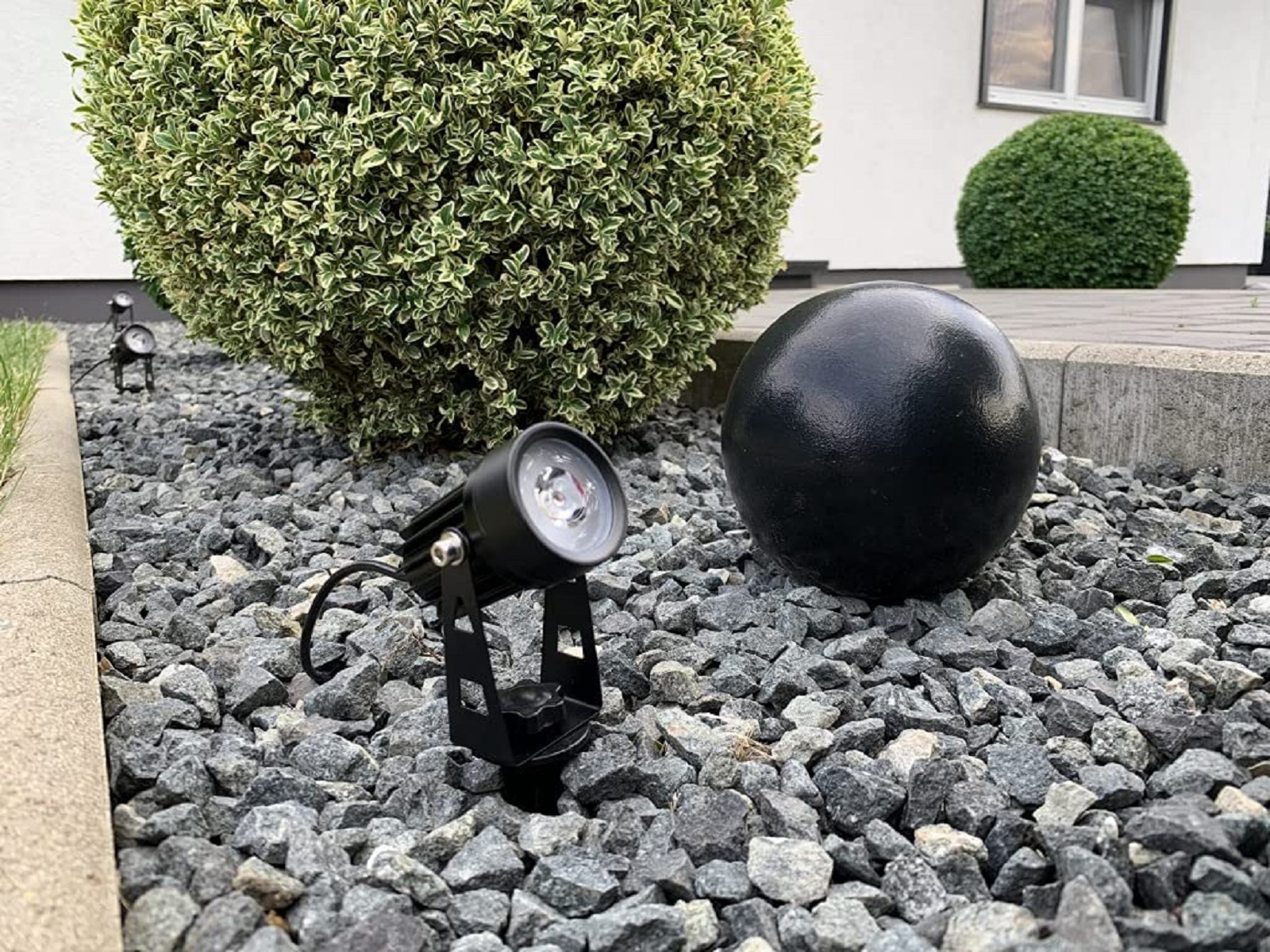Außenszene mit schwarzen Strahlern, einem schwarzen Ball und Grün auf Steinen.