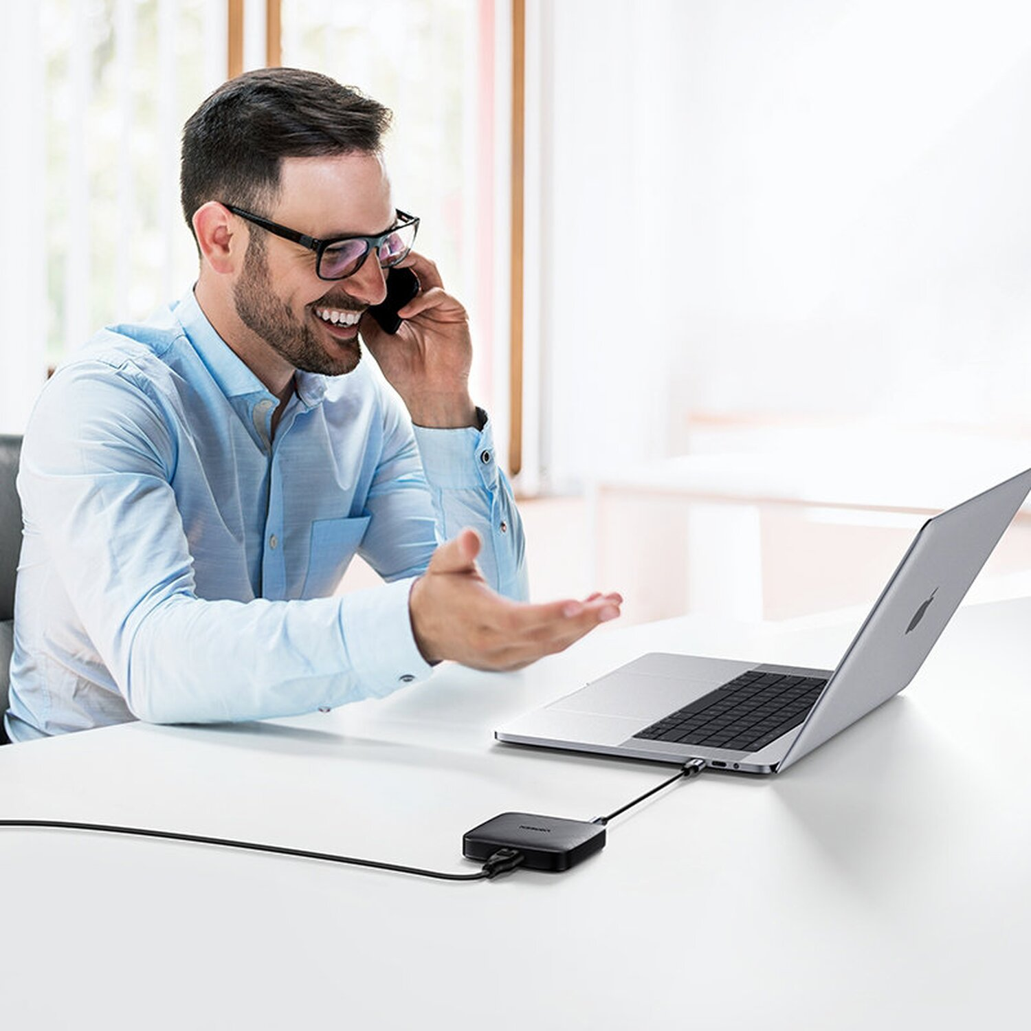 Mann telefoniert, nutzt Laptop mit angeschlossenem USB-Hub.