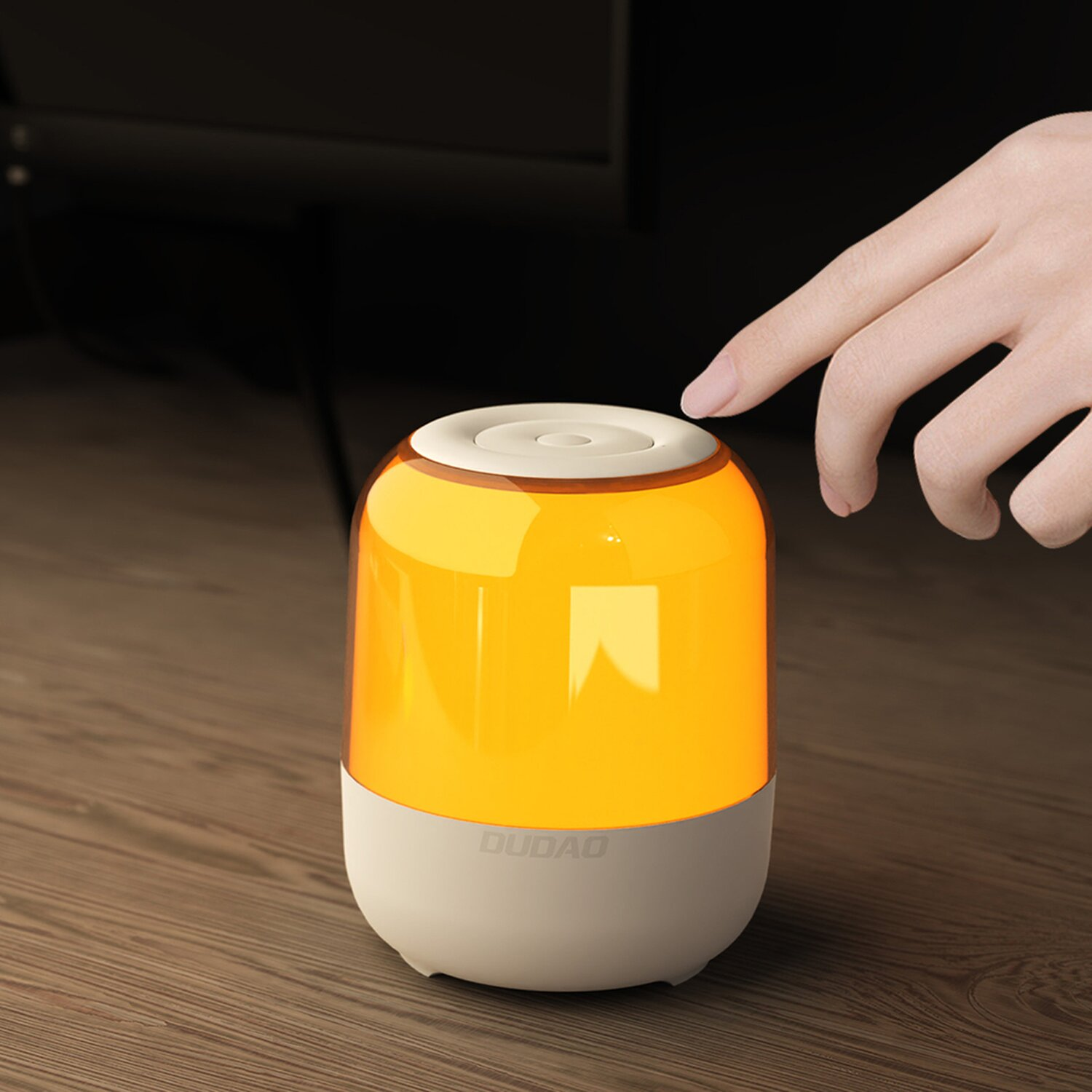 Eine Hand drückt auf eine orange leuchtende Lampe. Die Lampe ist weiß und orange, auf Holz.