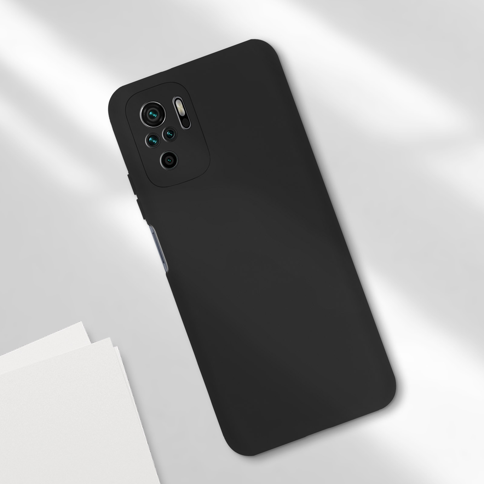 Una cover per telefono nera con modulo fotocamera è mostrata su una superficie bianca con due fogli bianchi.