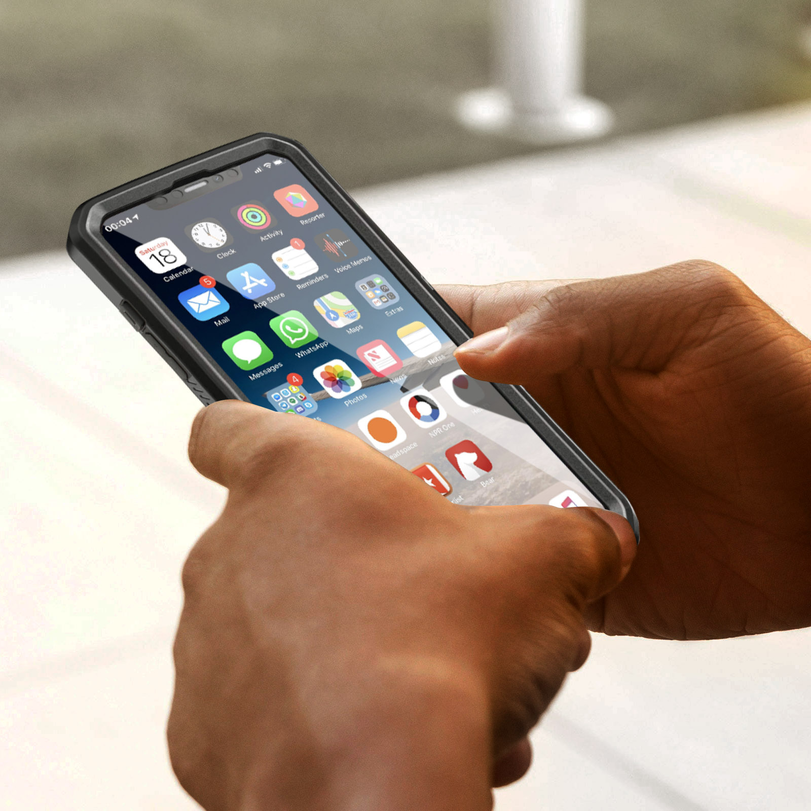 Una persona tiene in mano un telefono con una custodia nera, che mostra le icone delle app sullo schermo.