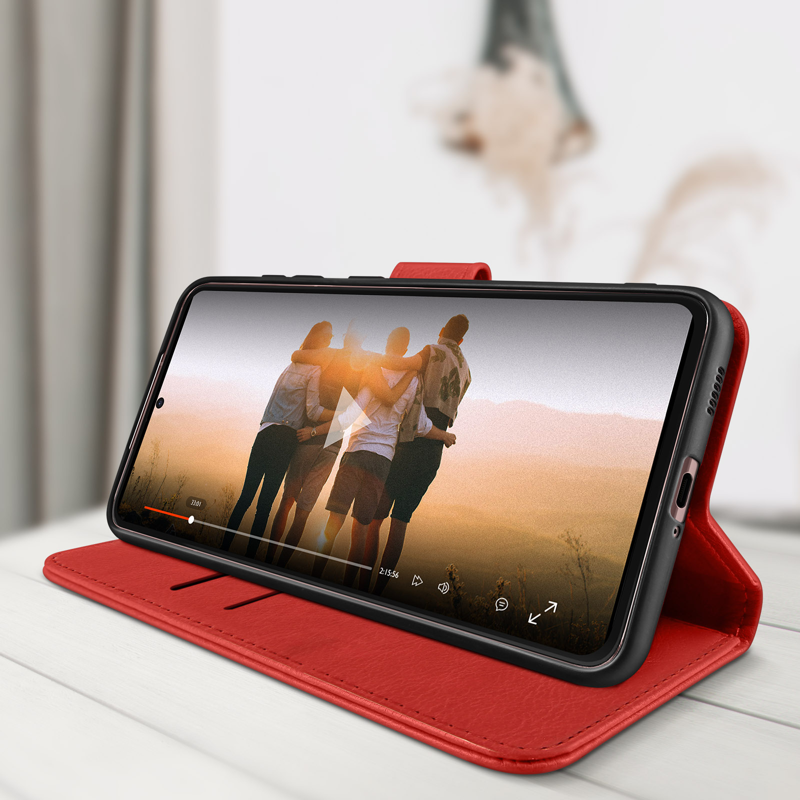 Étui de téléphone rouge avec un téléphone montrant une vidéo de personnes s'embrassant. Table blanche.