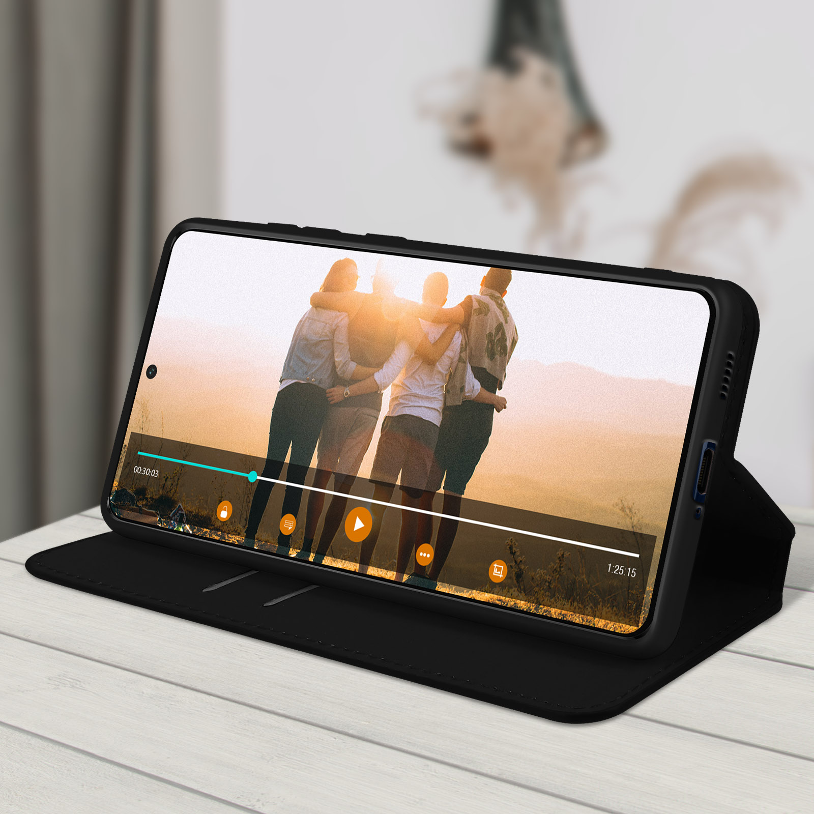Un téléphone affiche une vidéo de personnes s'embrassant, dans un étui noir sur une table en bois.
