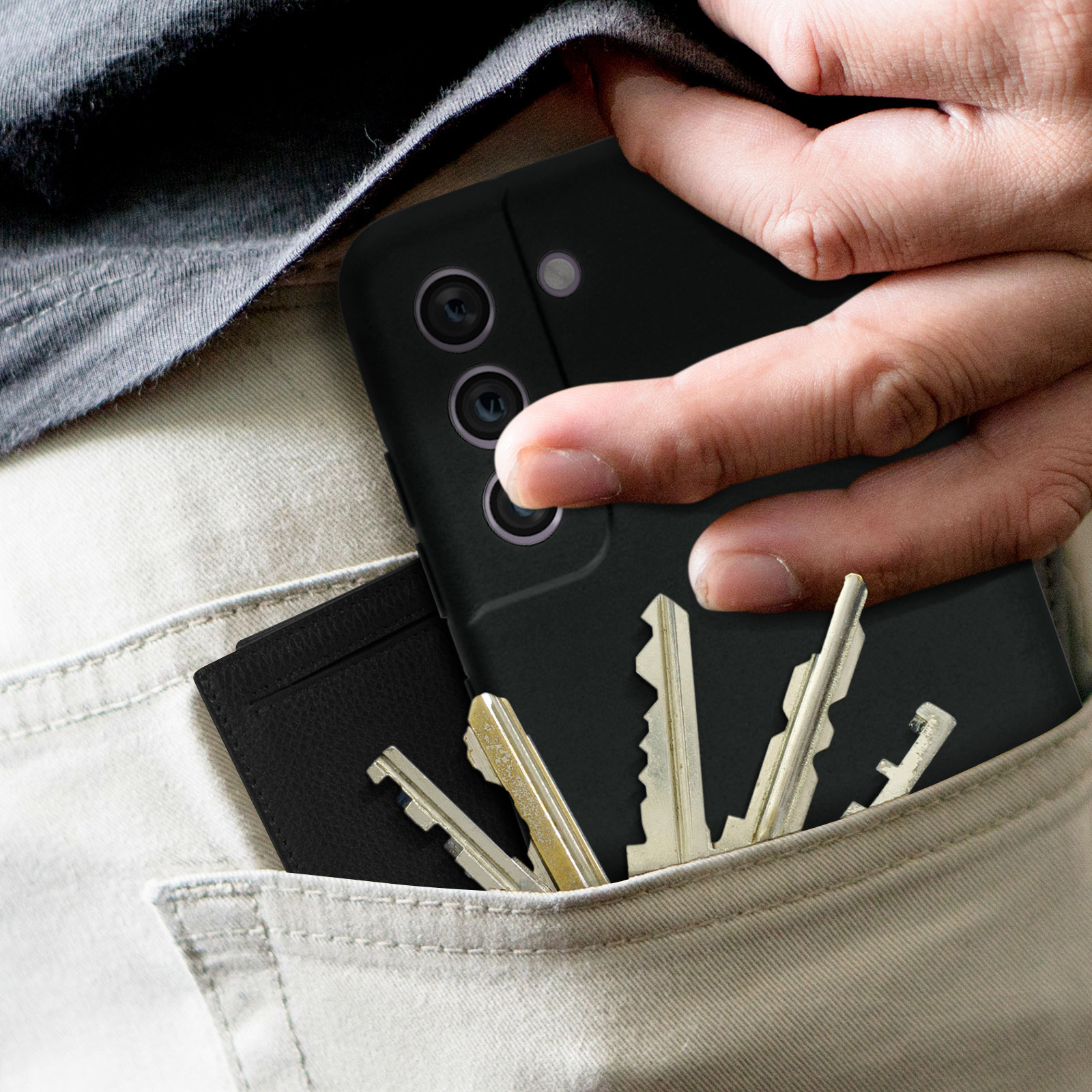 Main avec des clés et un portefeuille dans une poche, avec une coque de téléphone noire.