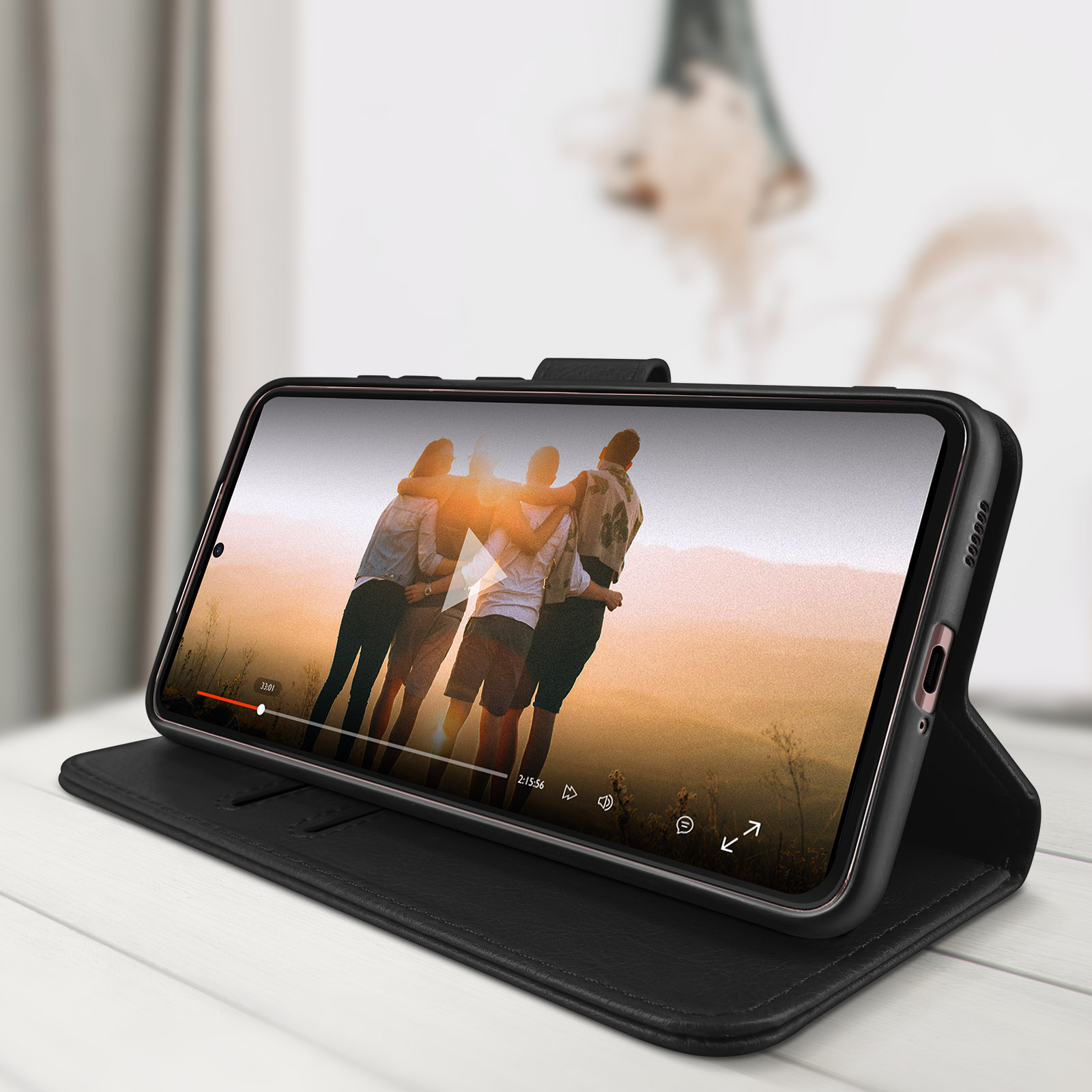 Téléphone affichant une vidéo, dans un étui noir ouvert. Arrière-plan flou, montrant des personnes.