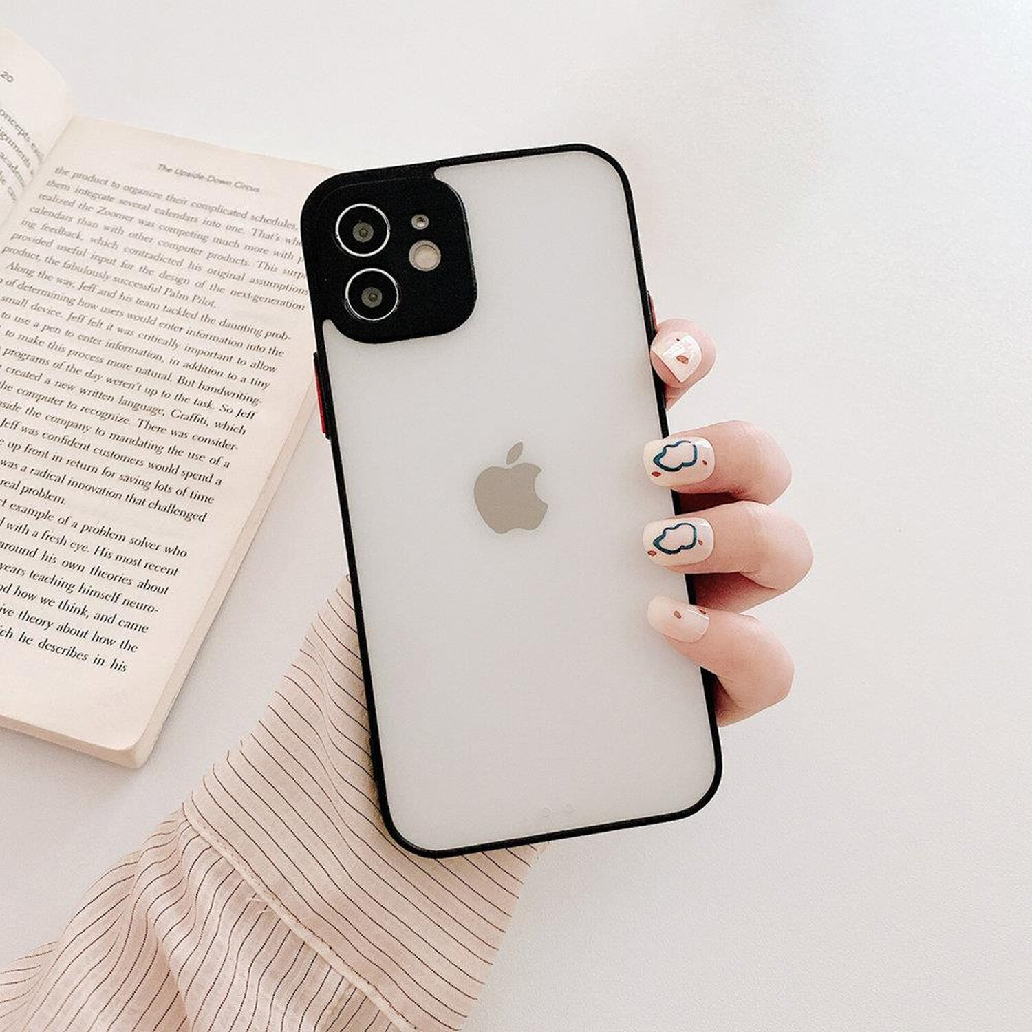 Hand hält Telefon in klarer Hülle, Buch im Hintergrund.