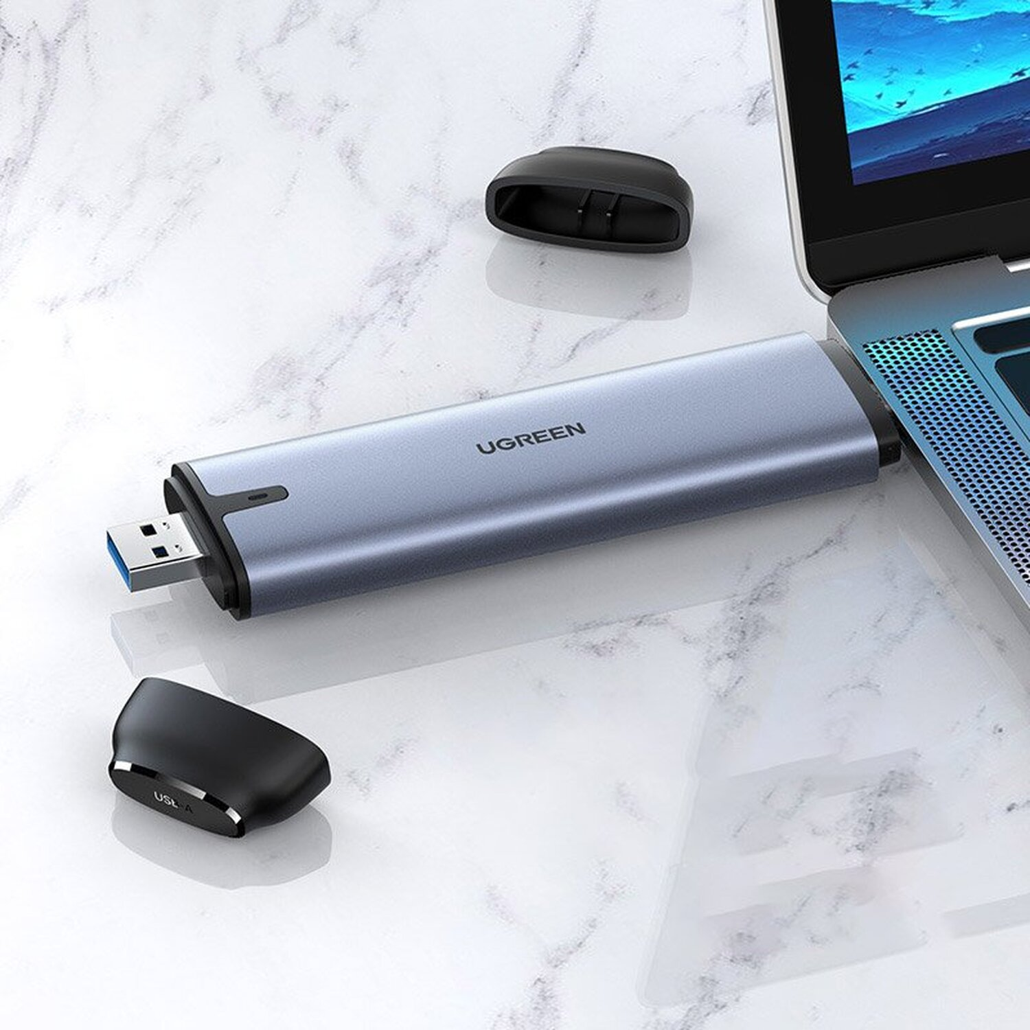 Ein blauer UGREEN USB-C-Hub neben einem Laptop. Zwei schwarze Kappen sind ebenfalls vorhanden.