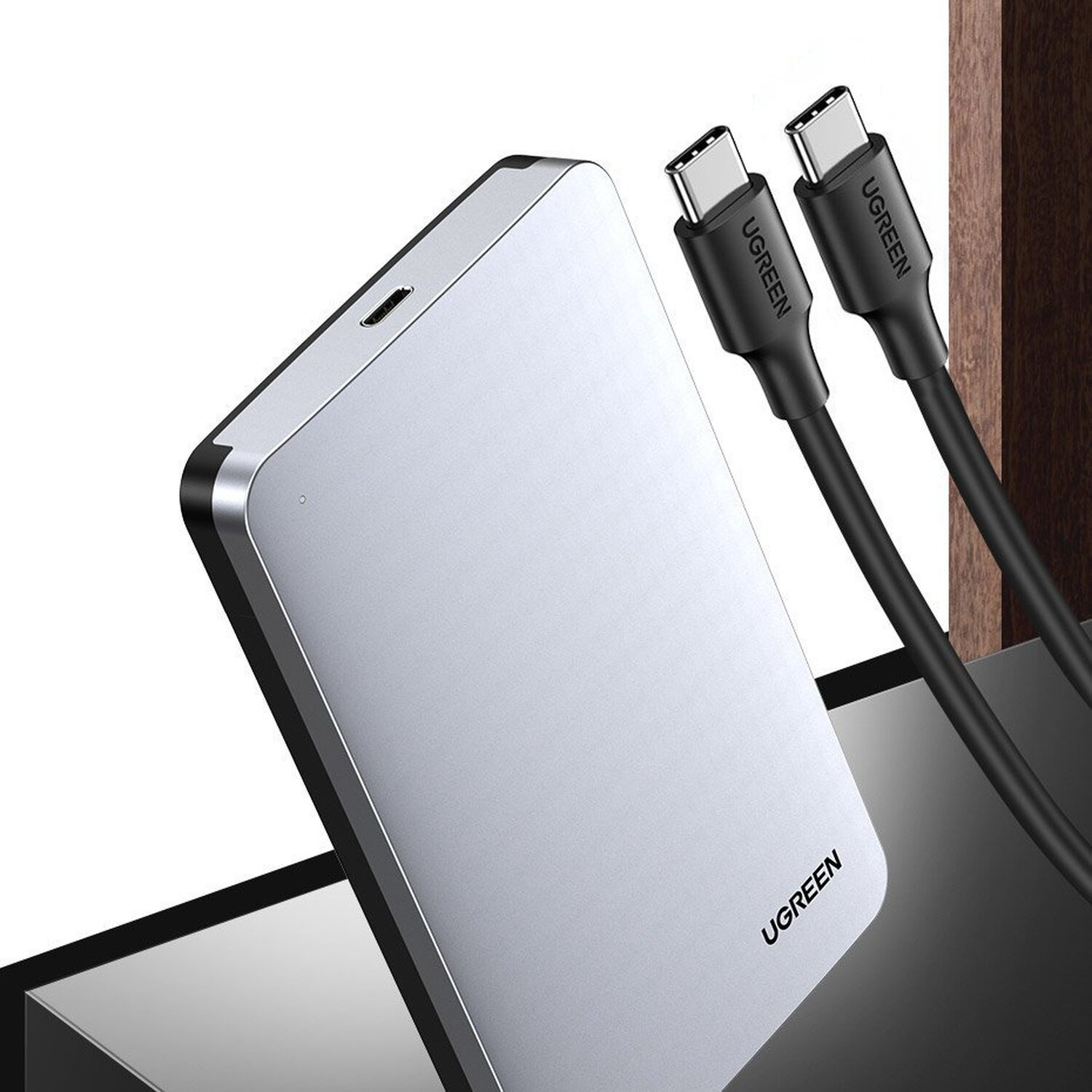 Eine silberne externe Festplatte mit zwei schwarzen USB-C-Kabeln auf heller Oberfläche.