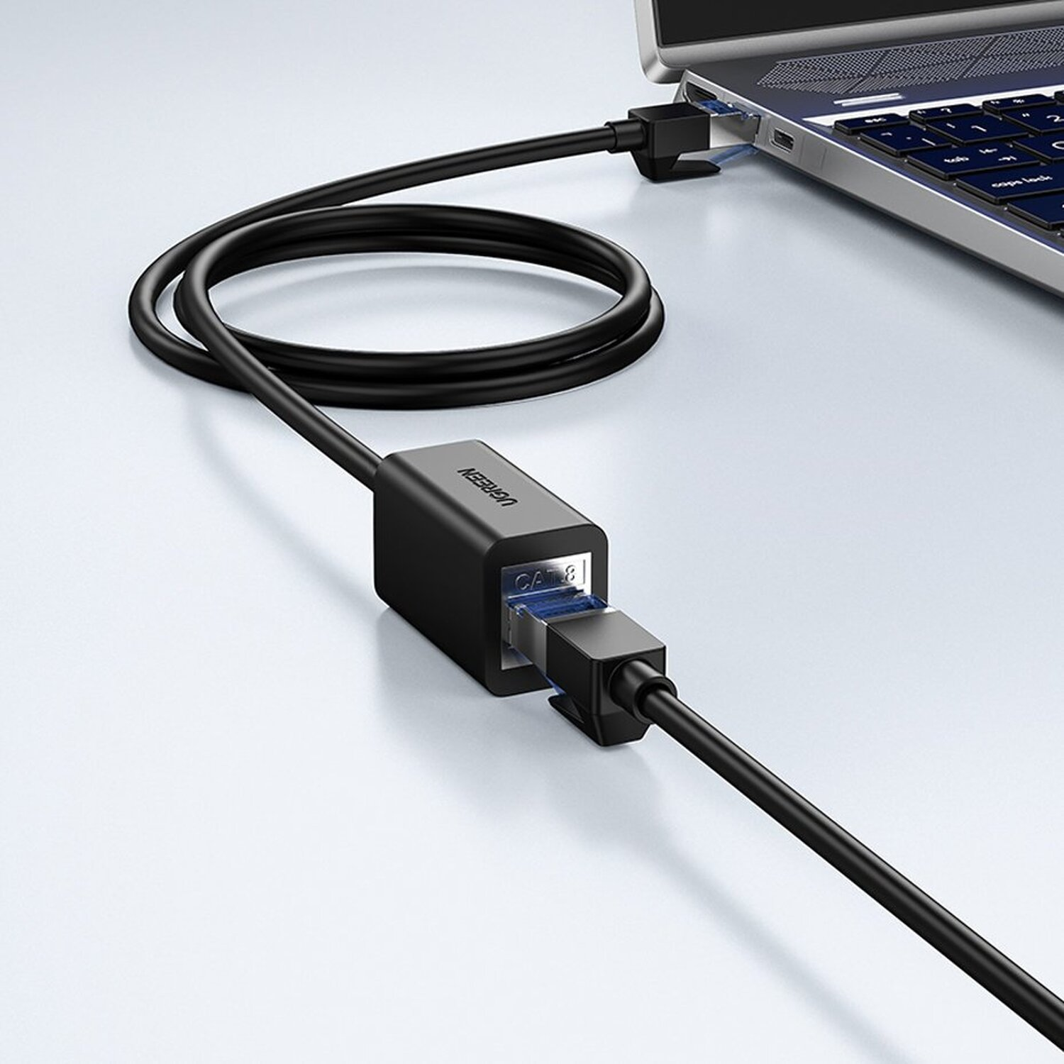 Schwarzes UGREEN CAT6-Kabel, an Laptop und Adapter angeschlossen. Weiße Oberfläche.