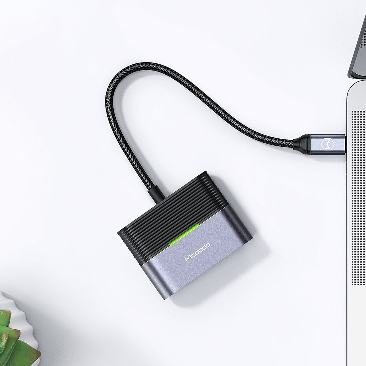 Ein grauer Adapter, der mit einem Laptop mit schwarzem geflochtenem Kabel auf weißer Oberfläche verbunden ist.