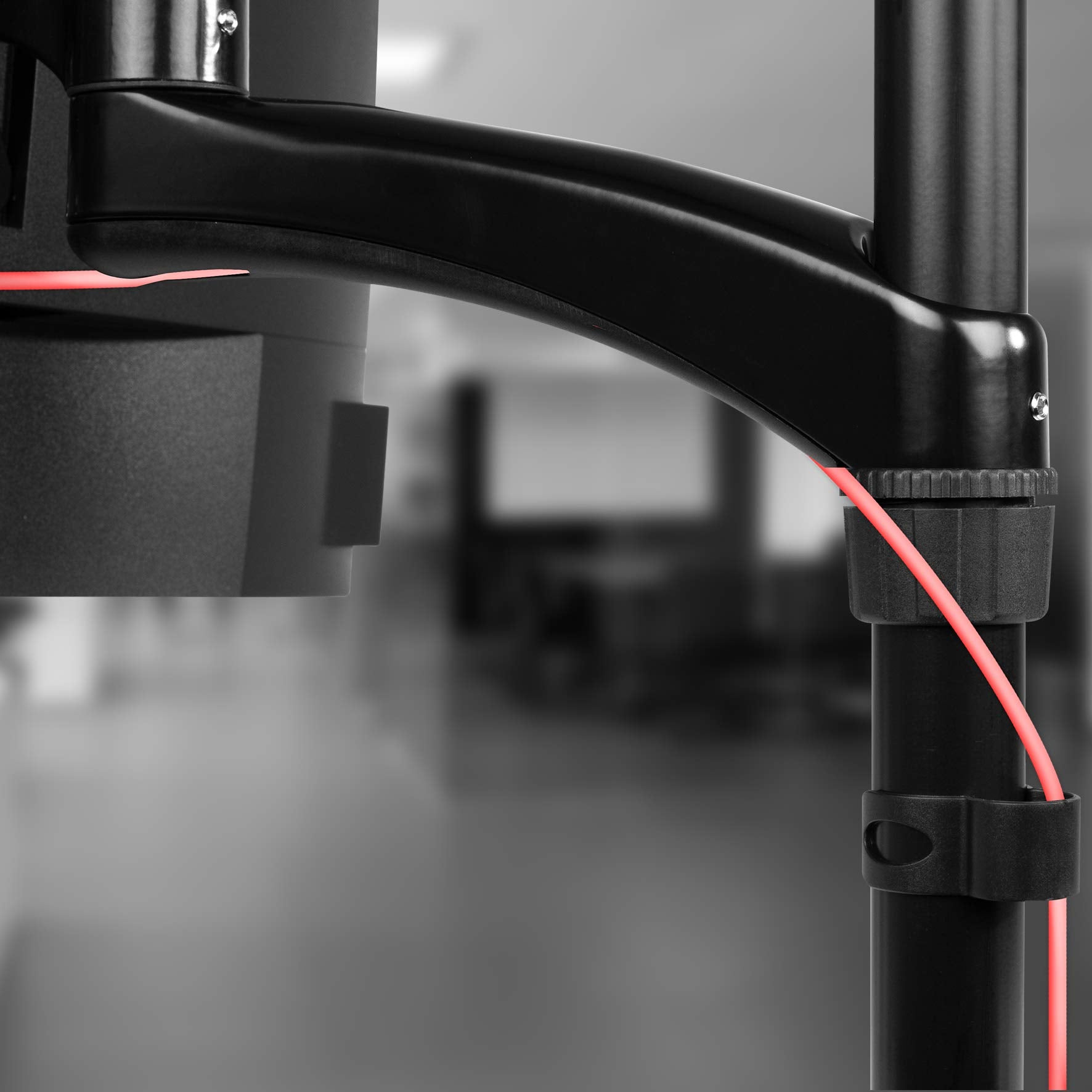 Nahaufnahme eines schwarzen Monitorarms mit rotem Kabel auf unscharfem Hintergrund.