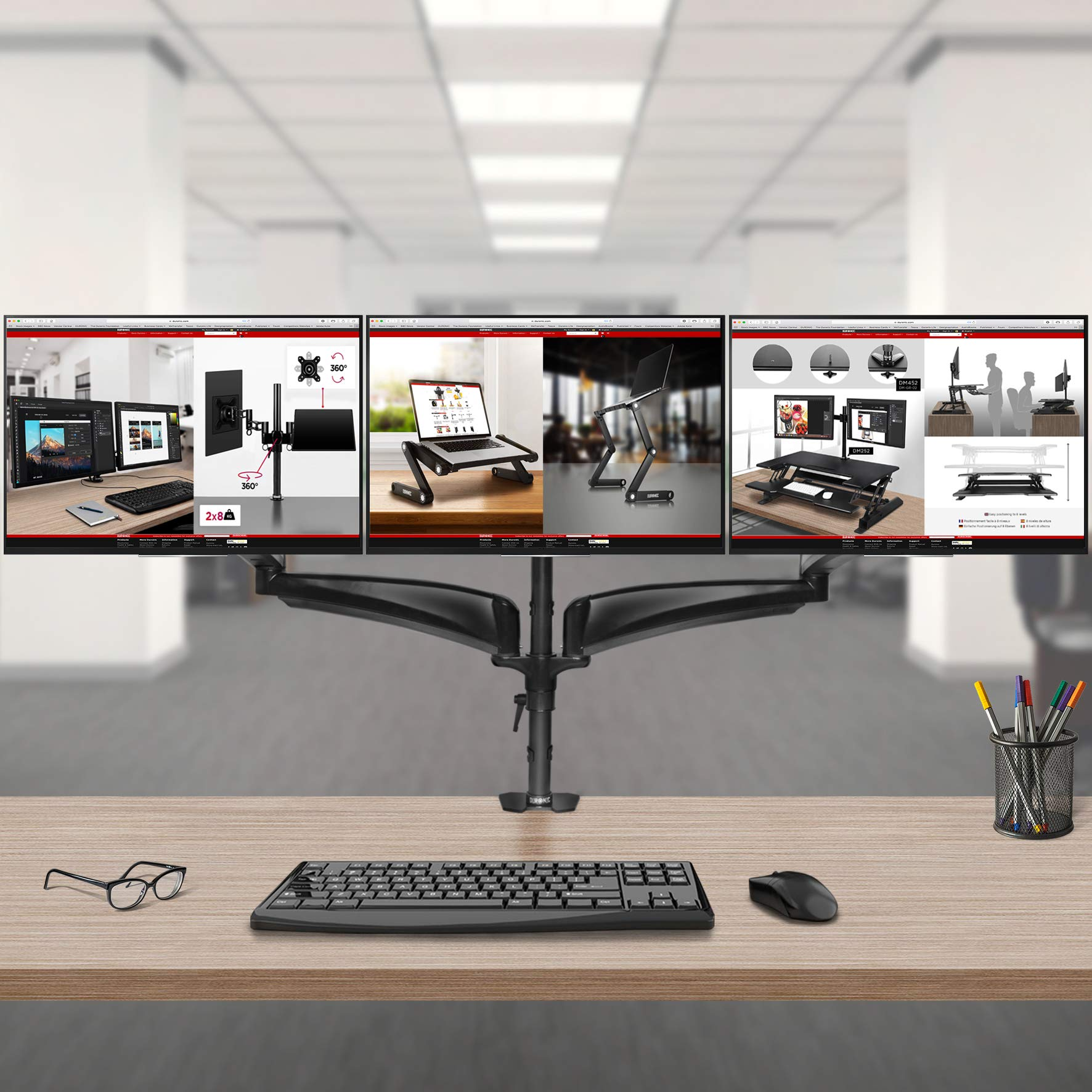 Tres monitores de computadora en un escritorio con accesorios y un fondo de oficina borroso.