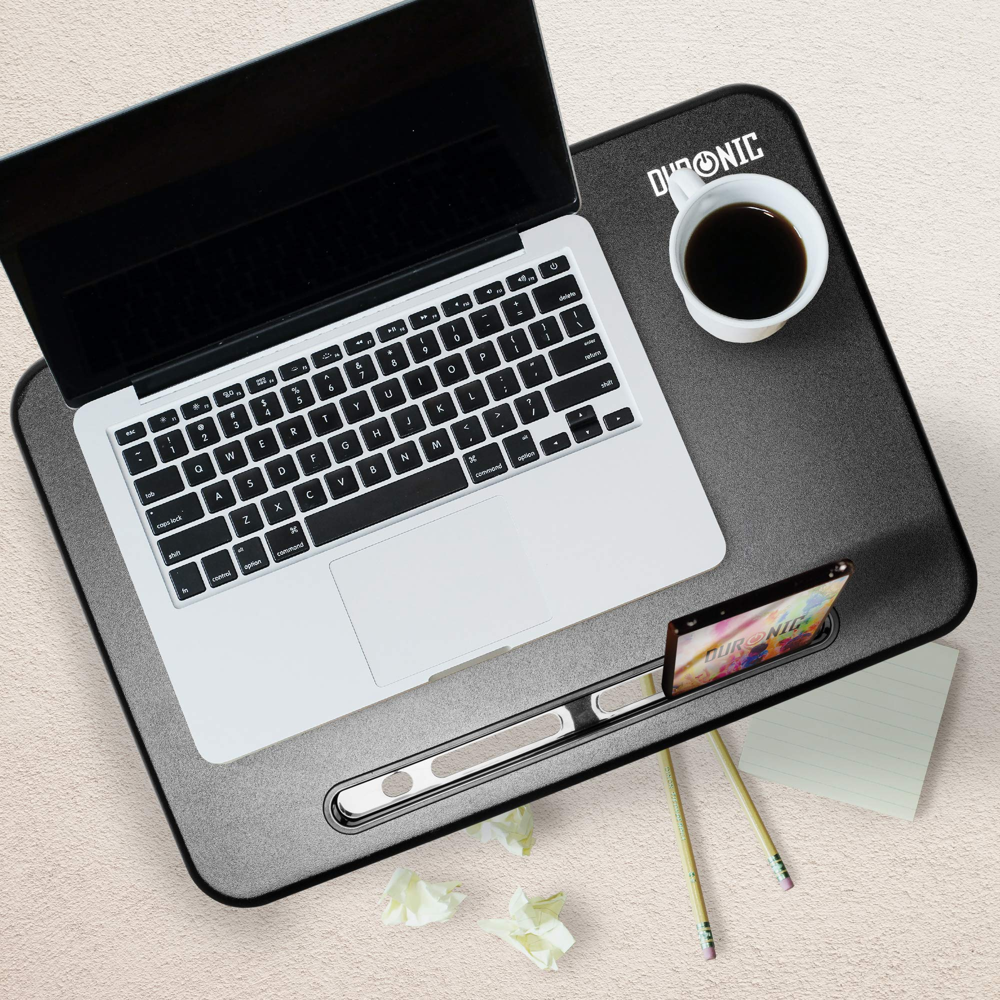 Ein Laptop auf einem schwarz-grauen Schoßschreibtisch. Eine Tasse Kaffee, Telefon und Bleistifte sind darauf.
