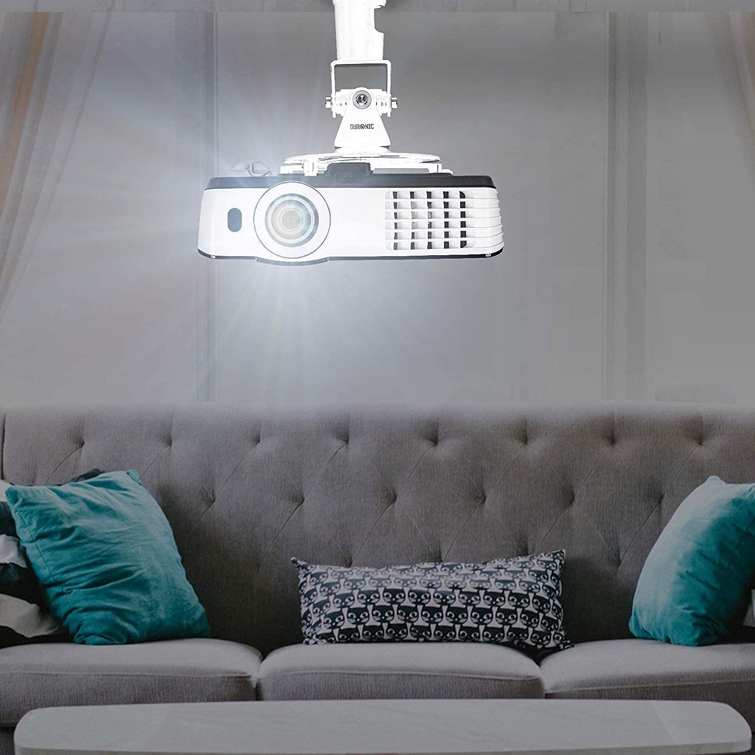 Un proyector blanco montado en el techo que proyecta luz sobre un sofá gris.