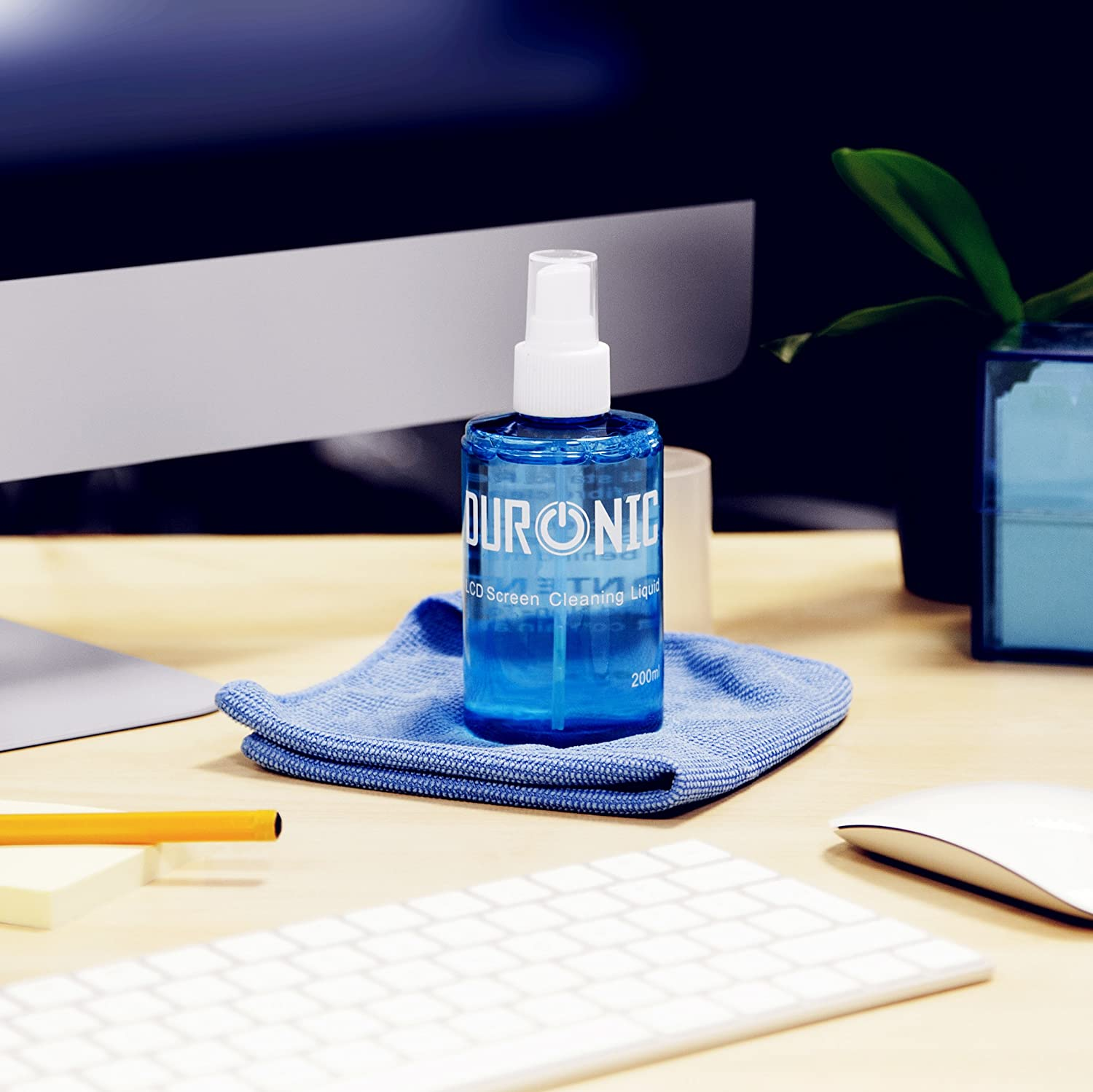Blaue Reinigungsflasche mit Tuch und Tastatur im Hintergrund.