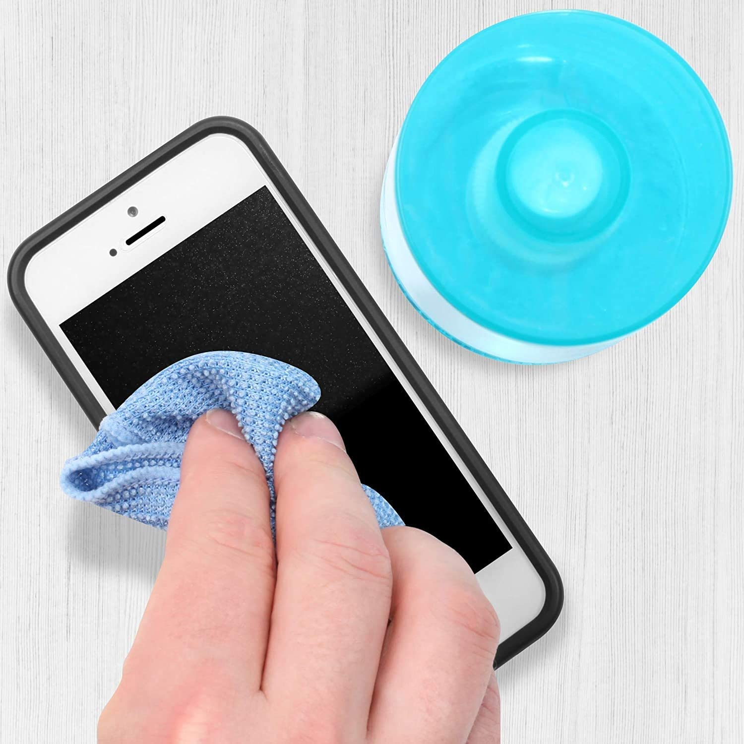 Hand reinigt Smartphone mit blauem Tuch und blauem Reinigungspad auf weißer Oberfläche.