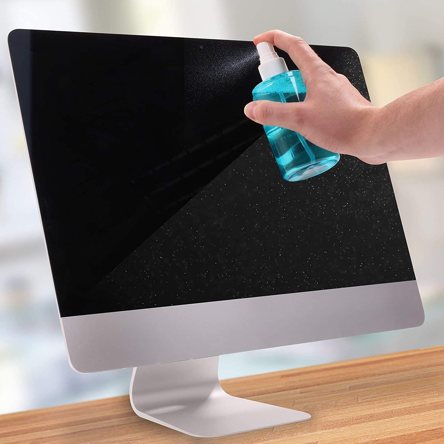 Person besprüht einen Monitorbildschirm mit Reinigungslösung. Weißer Hintergrund. Holzschreibtisch.