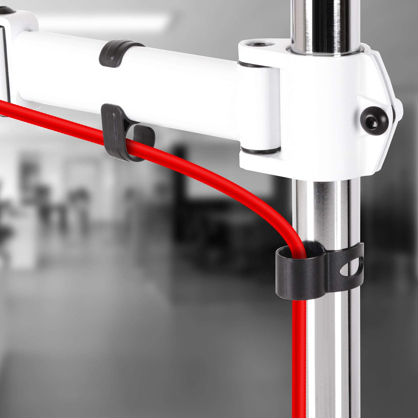 Nahaufnahme eines Monitorarms, ein rotes Kabel wird von schwarzen Clips gehalten.