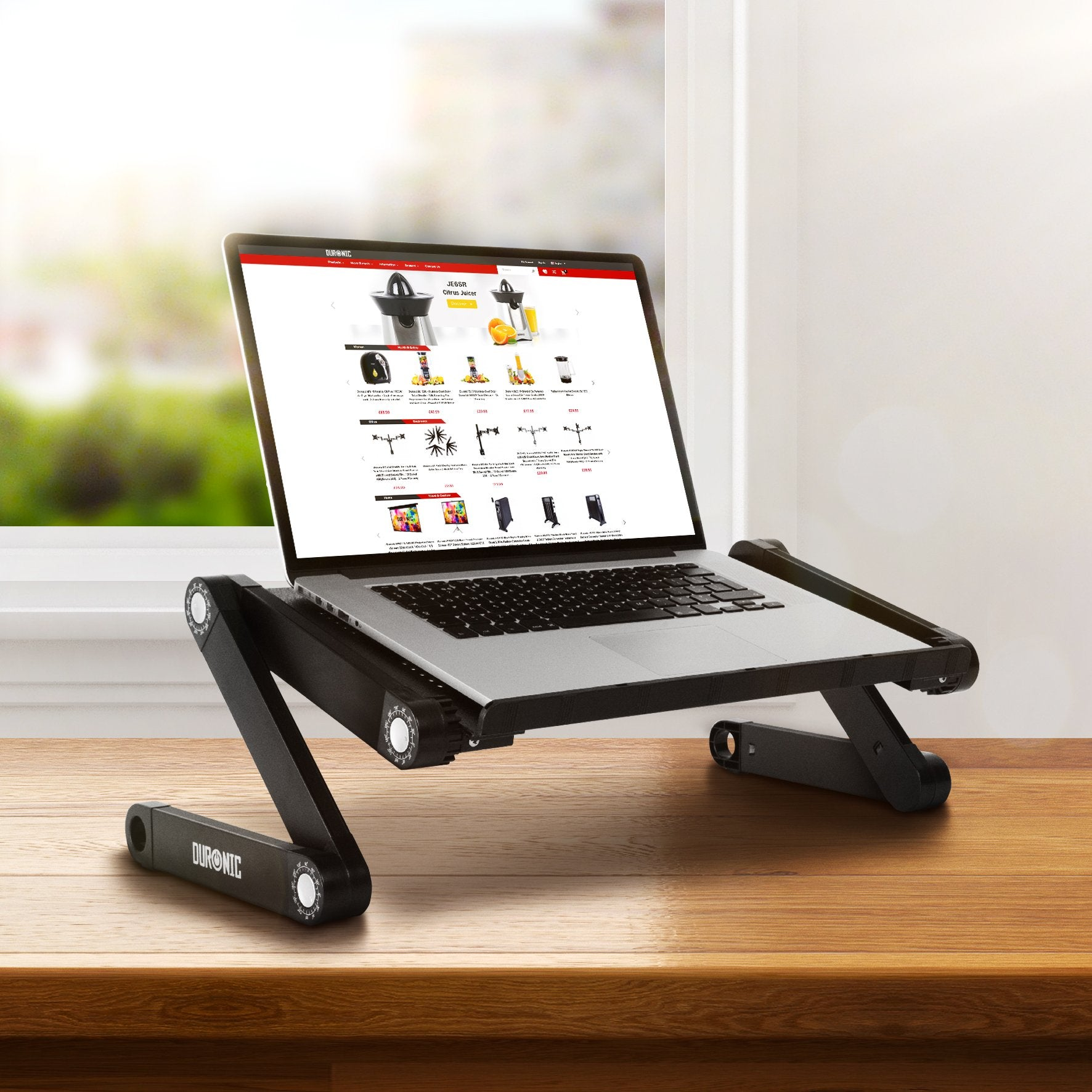 Un portátil en un soporte de escritorio ajustable negro sobre una mesa de madera.