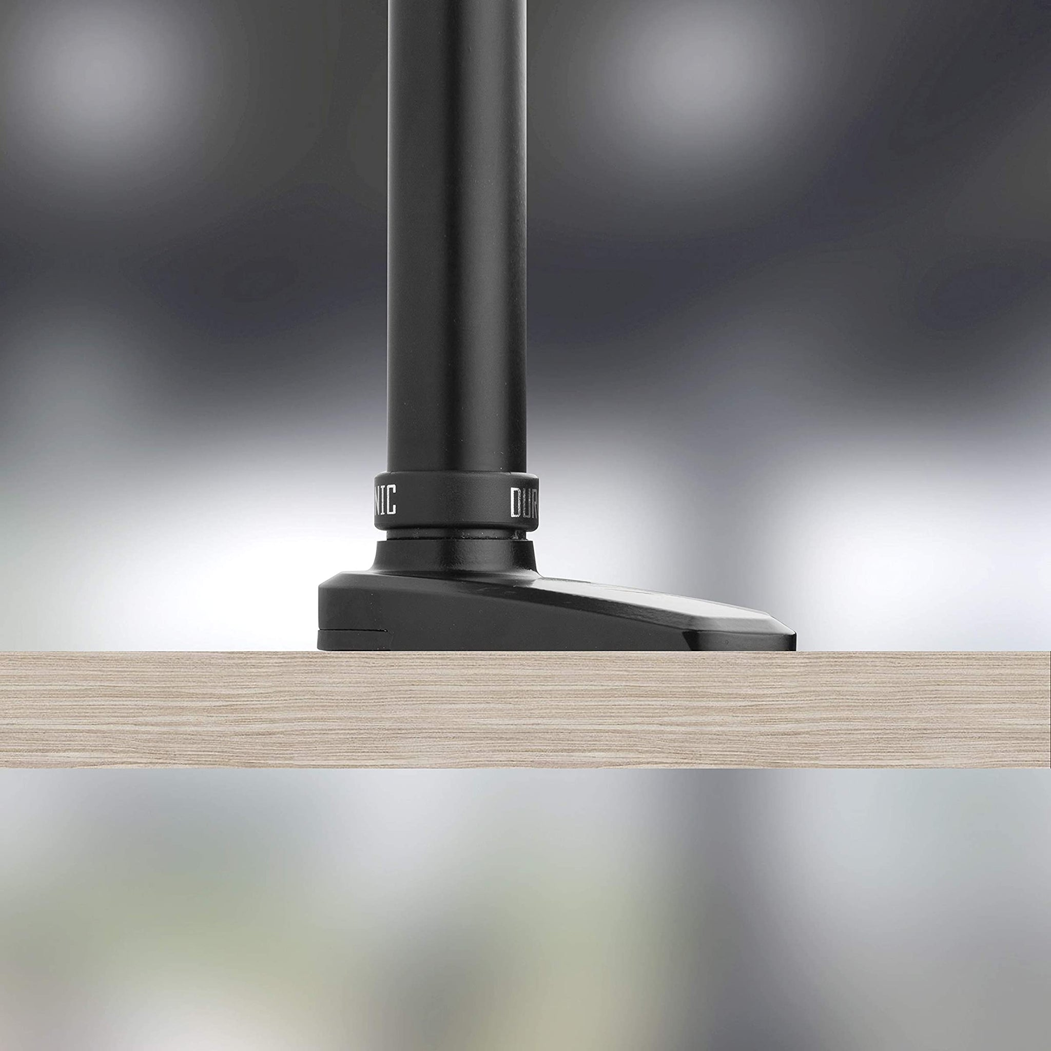 Base de soporte de monitor negro con poste negro adjunto, apoyado en una superficie de madera clara.