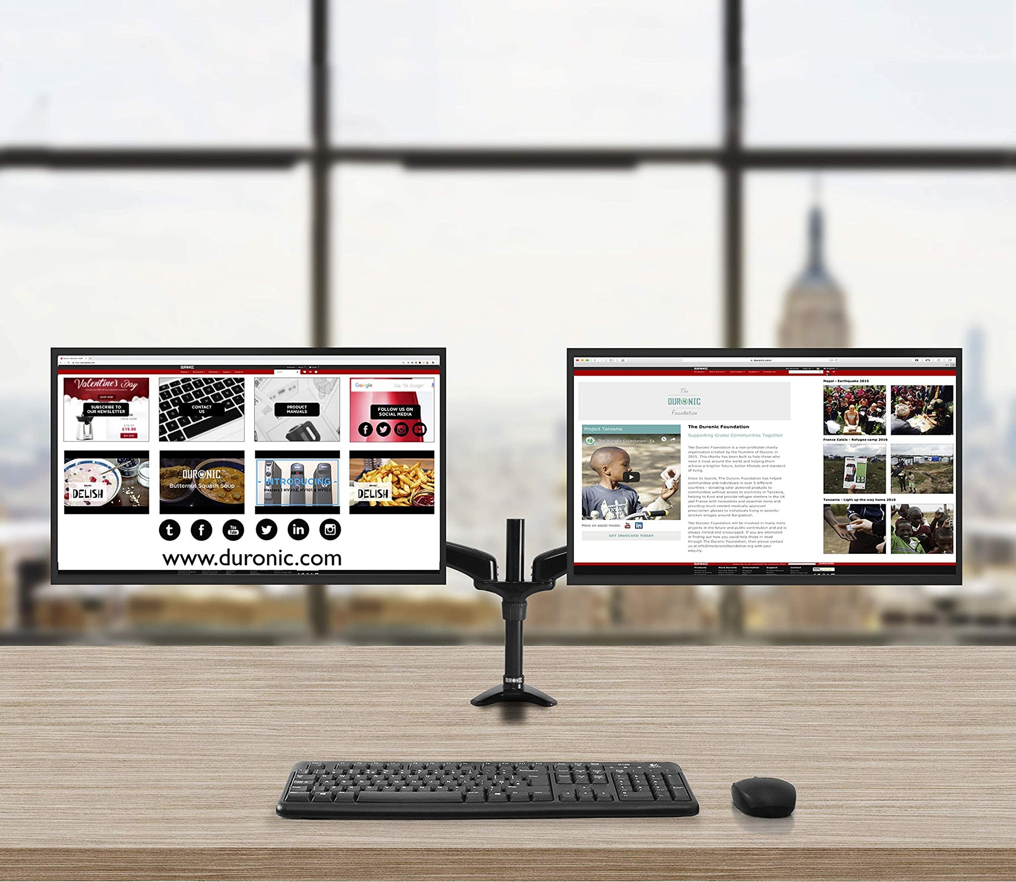 Un escritorio con dos monitores, un teclado y un ratón. Los monitores muestran páginas web con una ciudad de fondo.