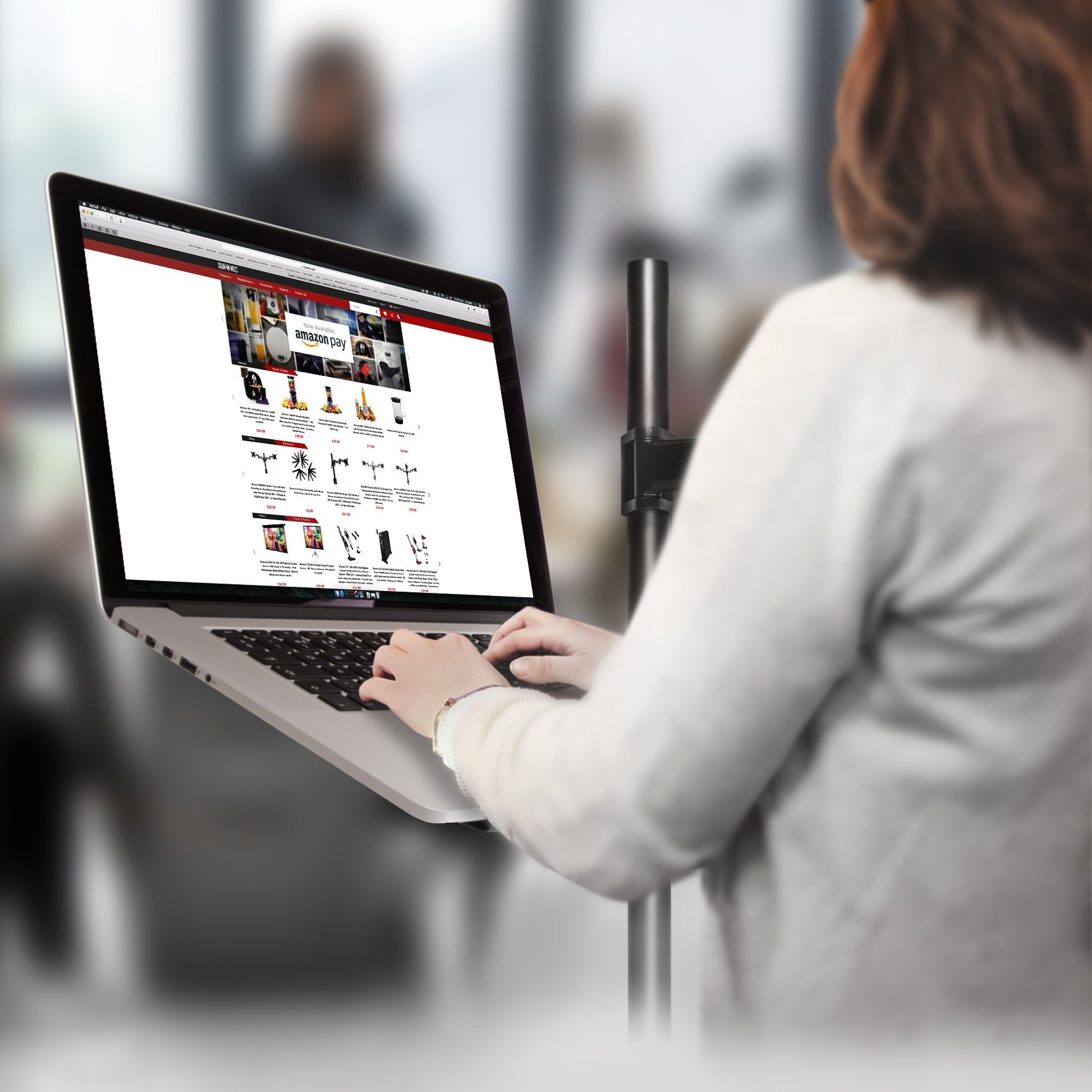 Una mujer usa una laptop conectada a un soporte de monitor, navegando por un sitio web.