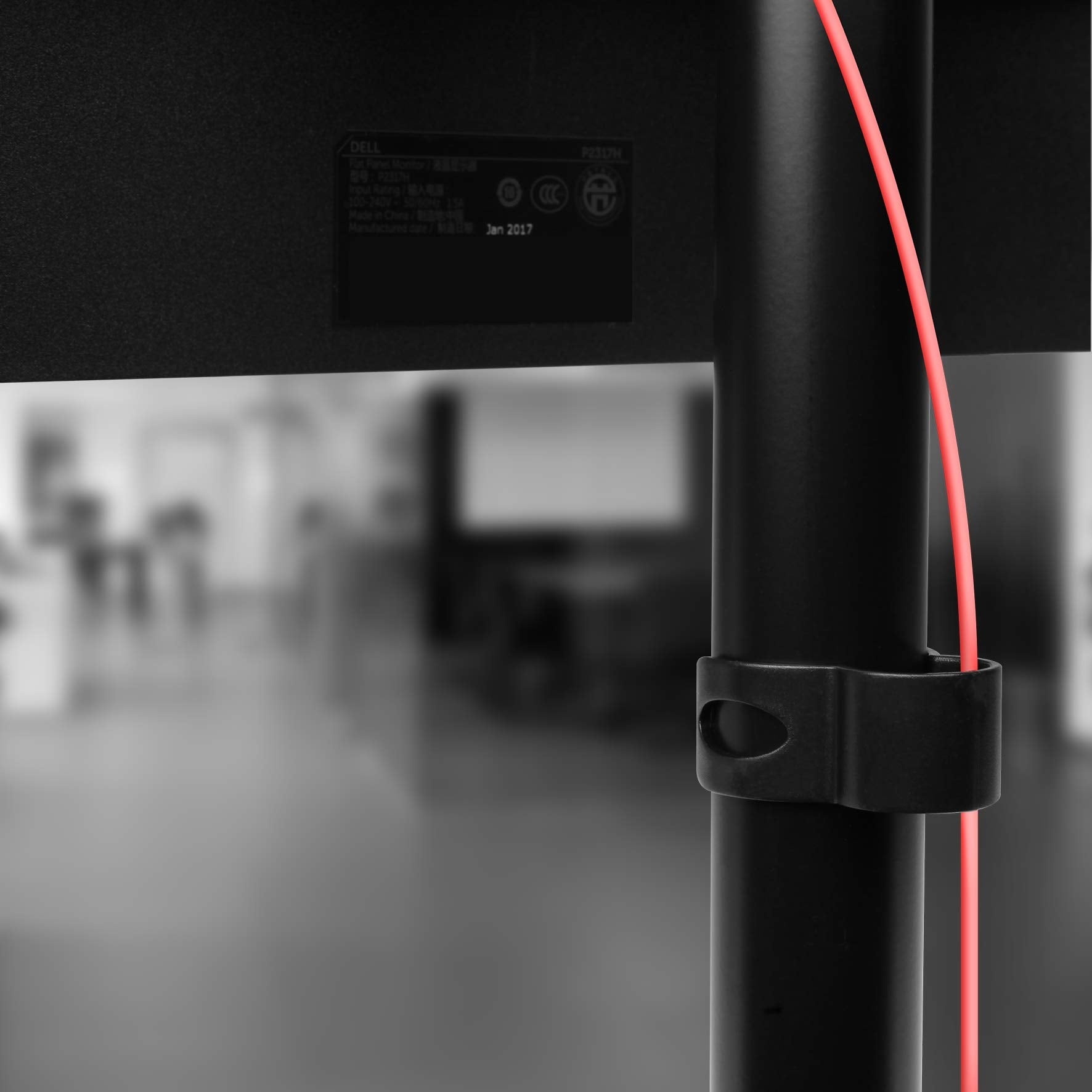 Schwarzer Monitorständer mit rotem Kabel. Der Bildschirm ist mit einem Bürohintergrund verschwommen.